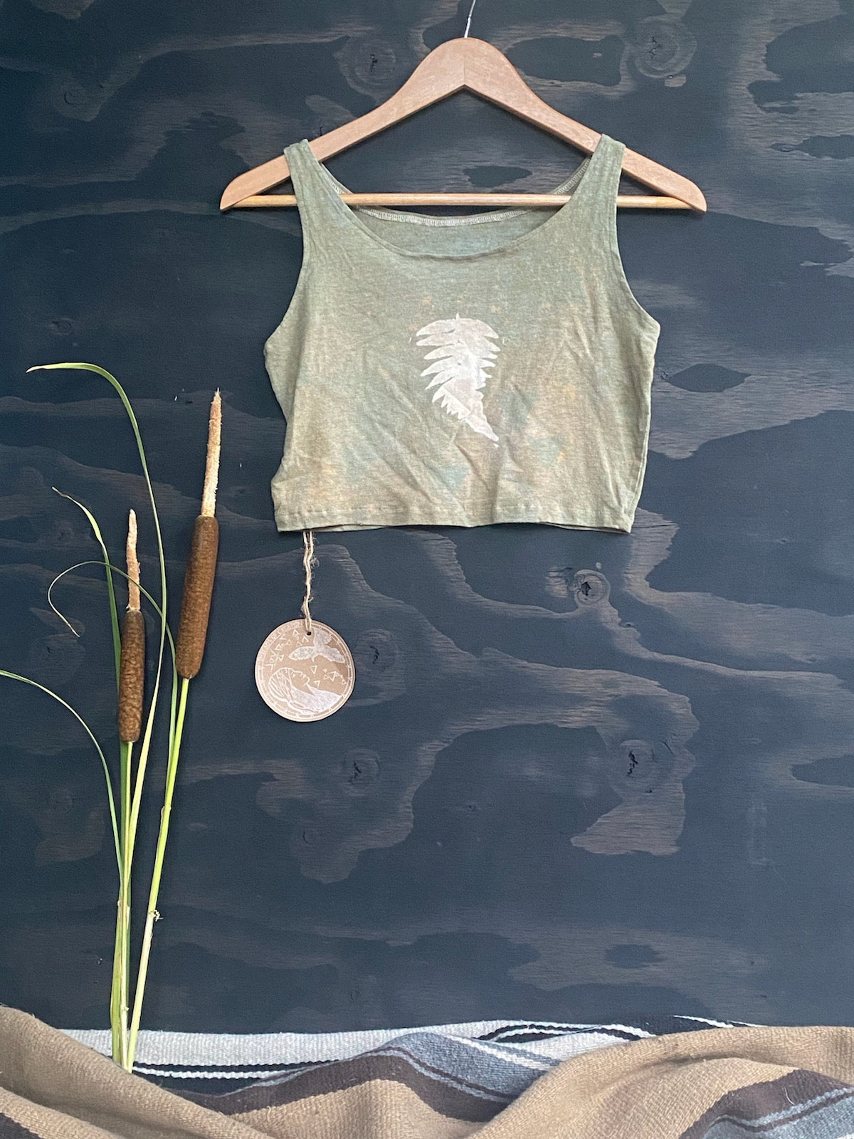 Teal Green Tank Top on a wooden hanger with a fern print against a black background