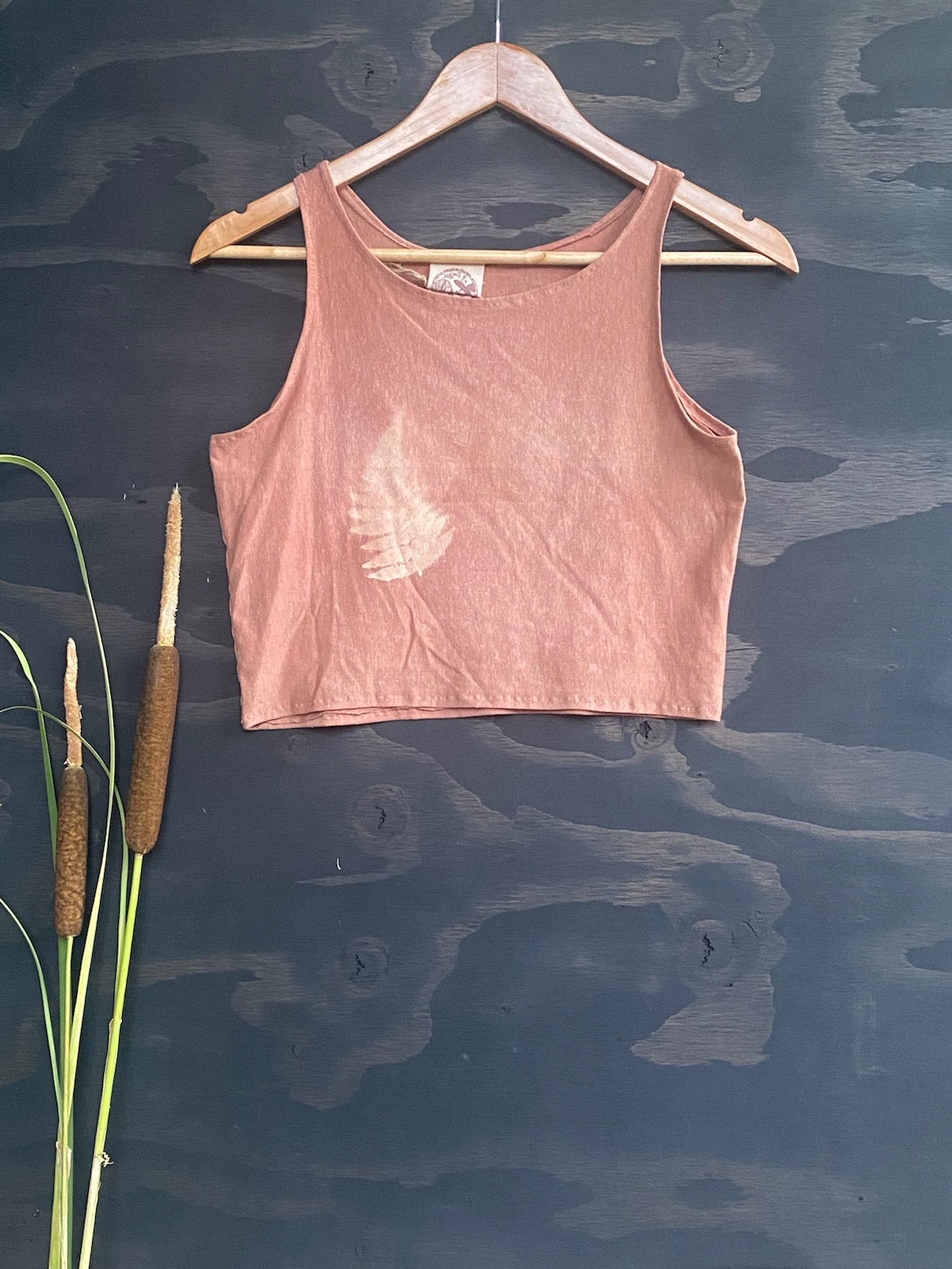 Black background with Rose Pink Tank Top with Printed Fern hanging on a wooden hanger