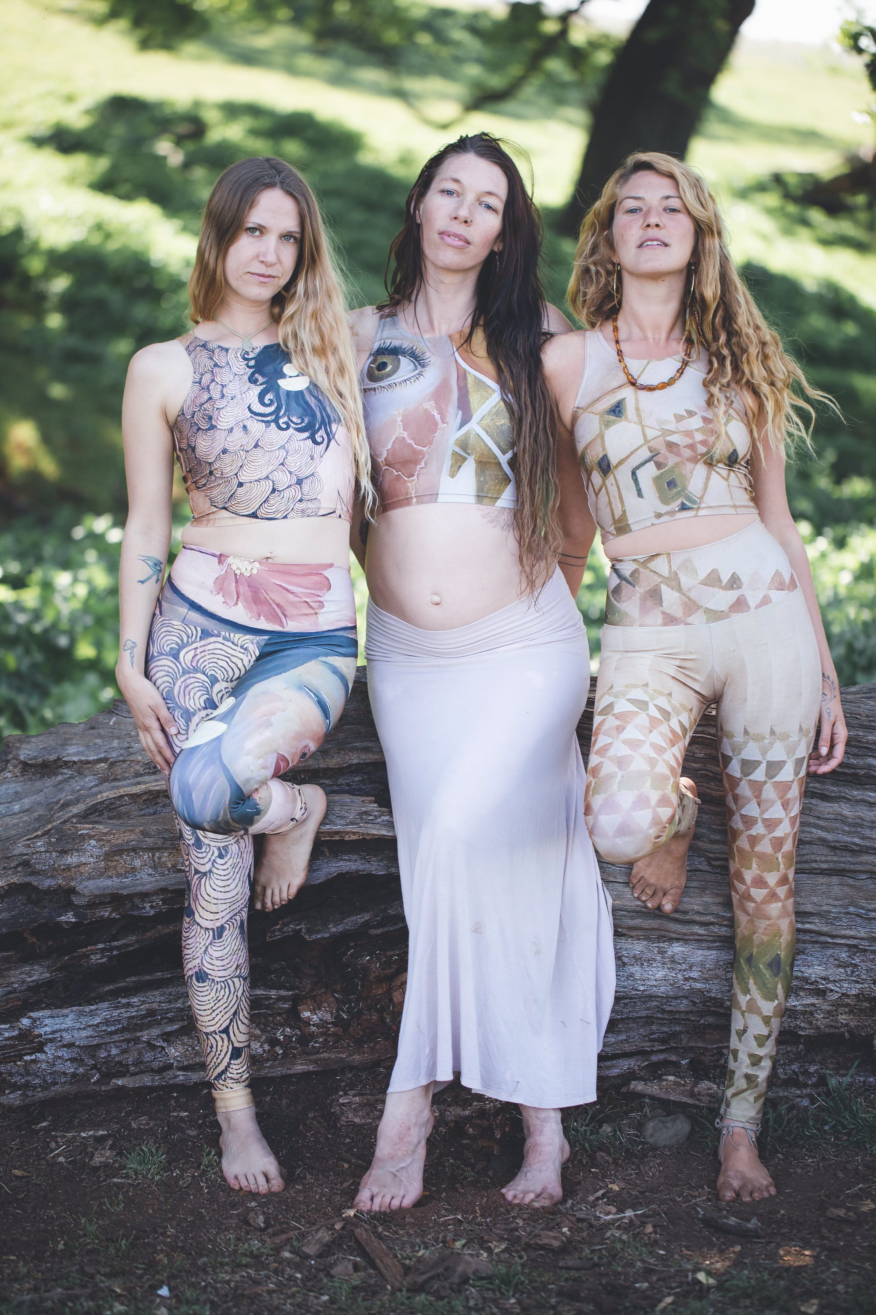 Three individuals posing outdoors, each wearing leggings with a different colorful geometric pattern, standing near a wooden structure in a natural setting.