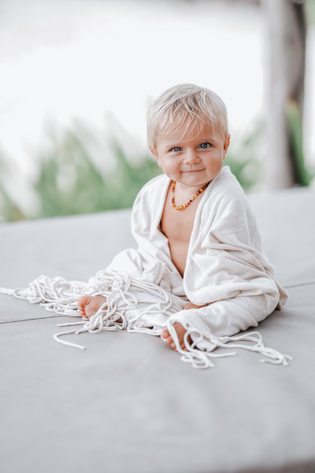 blonde haired baby wearing an amber necklace sitting and wrapped in a hemp naturally dyed kimono
