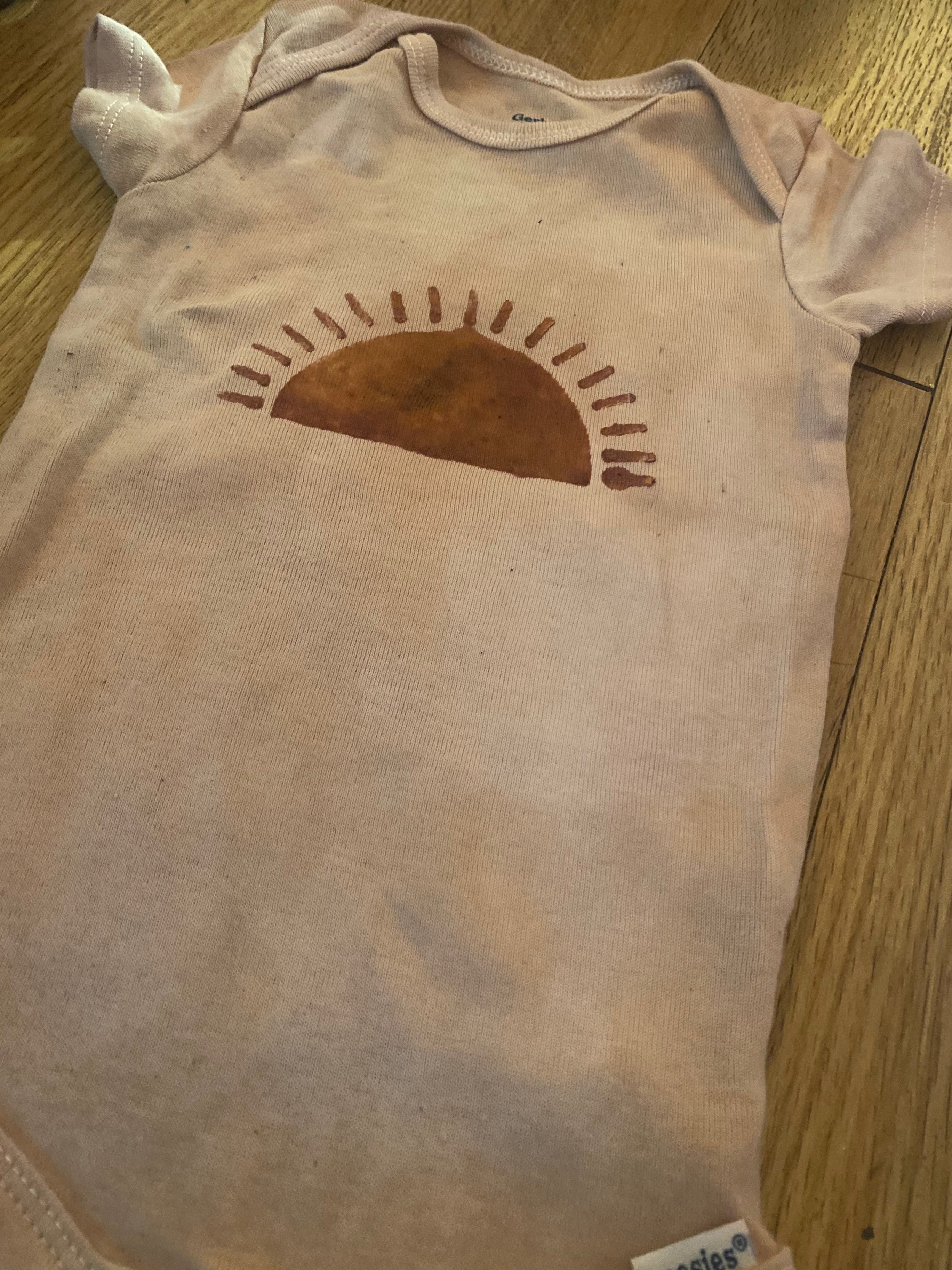 brown pink Baby onesie with a sun design on a wooden surface