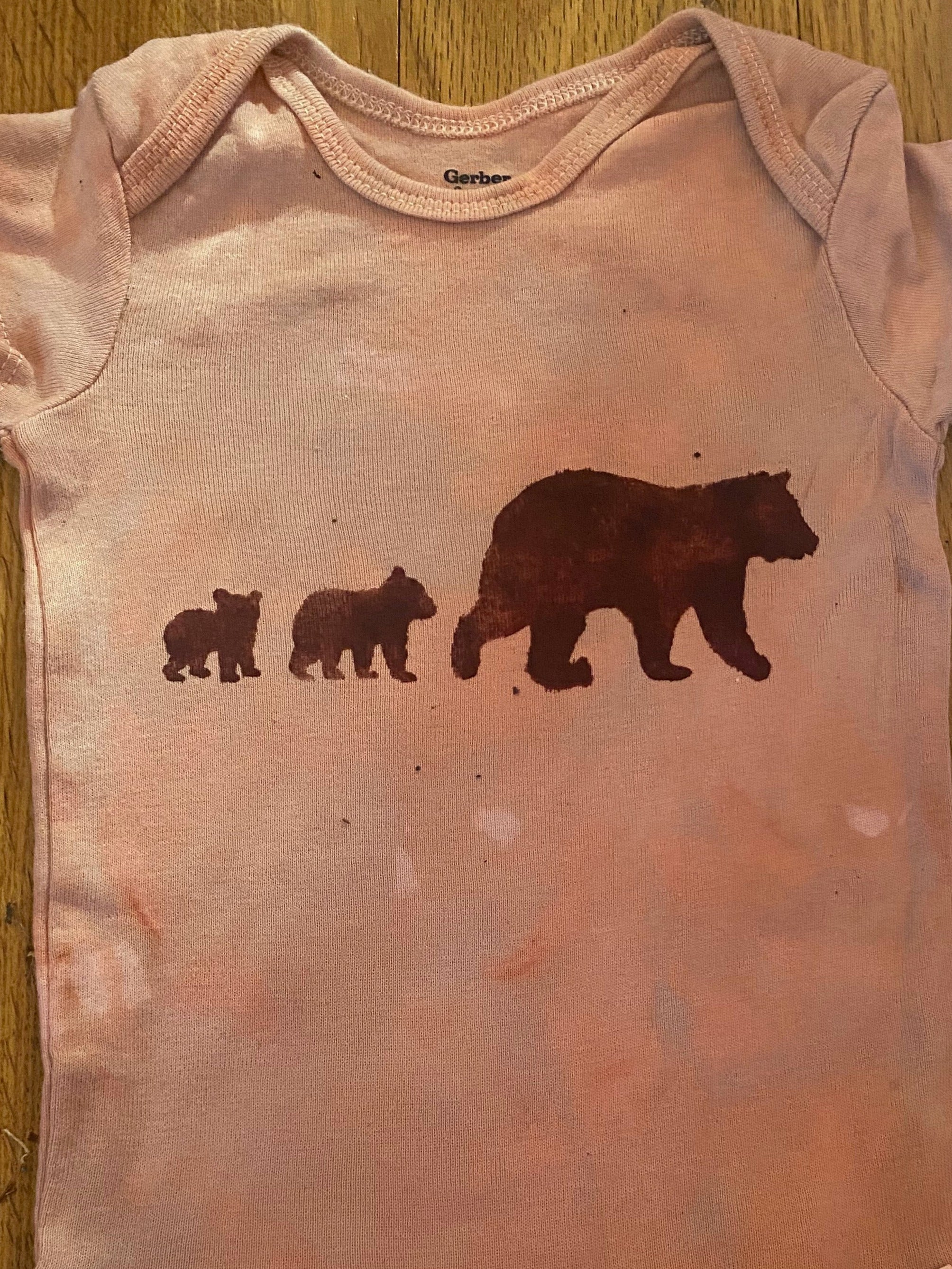 Pink baby onesie with bear illustrations on a wooden surface