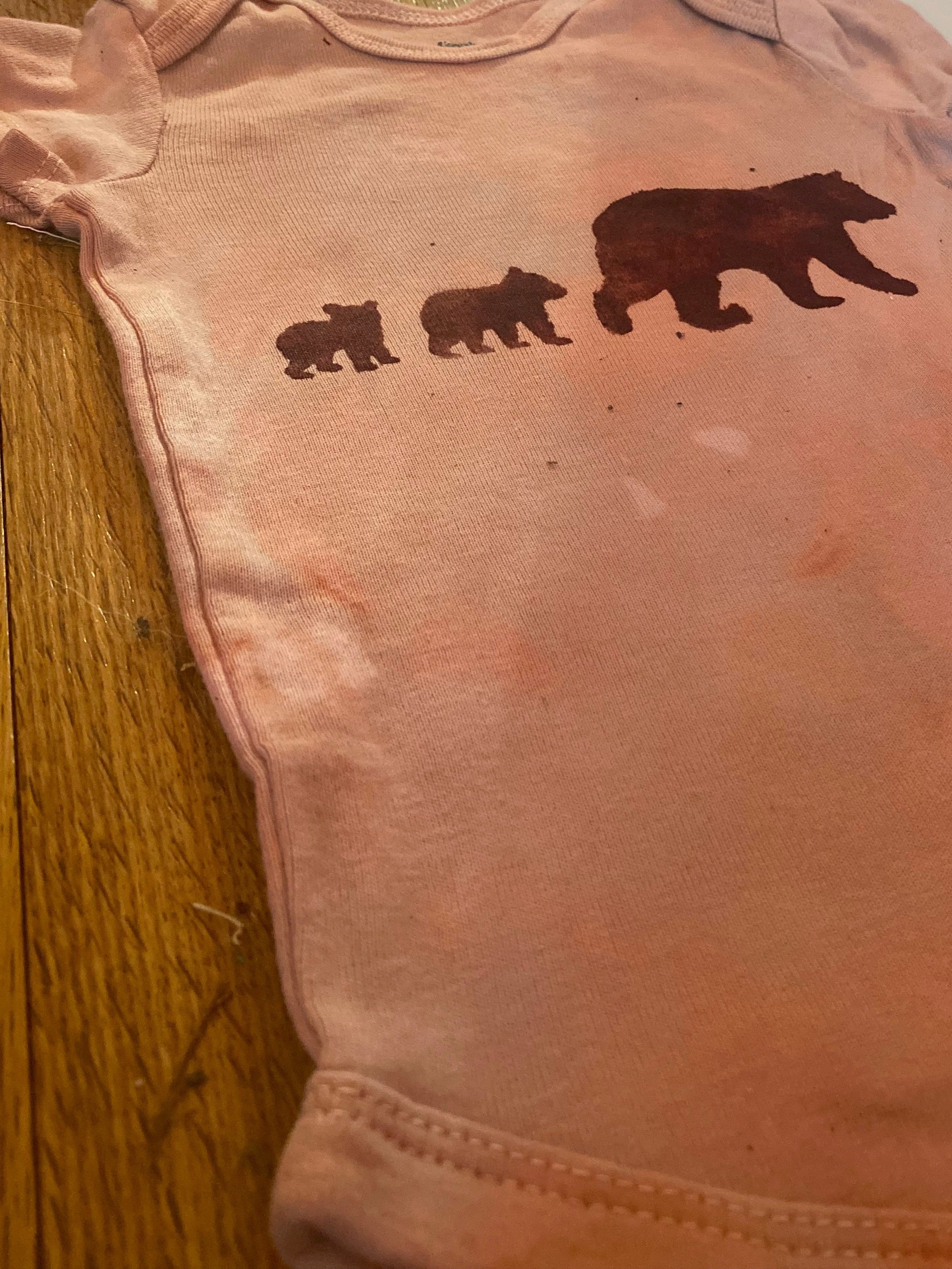 Pink baby onesie with bear illustrations on a wooden floor