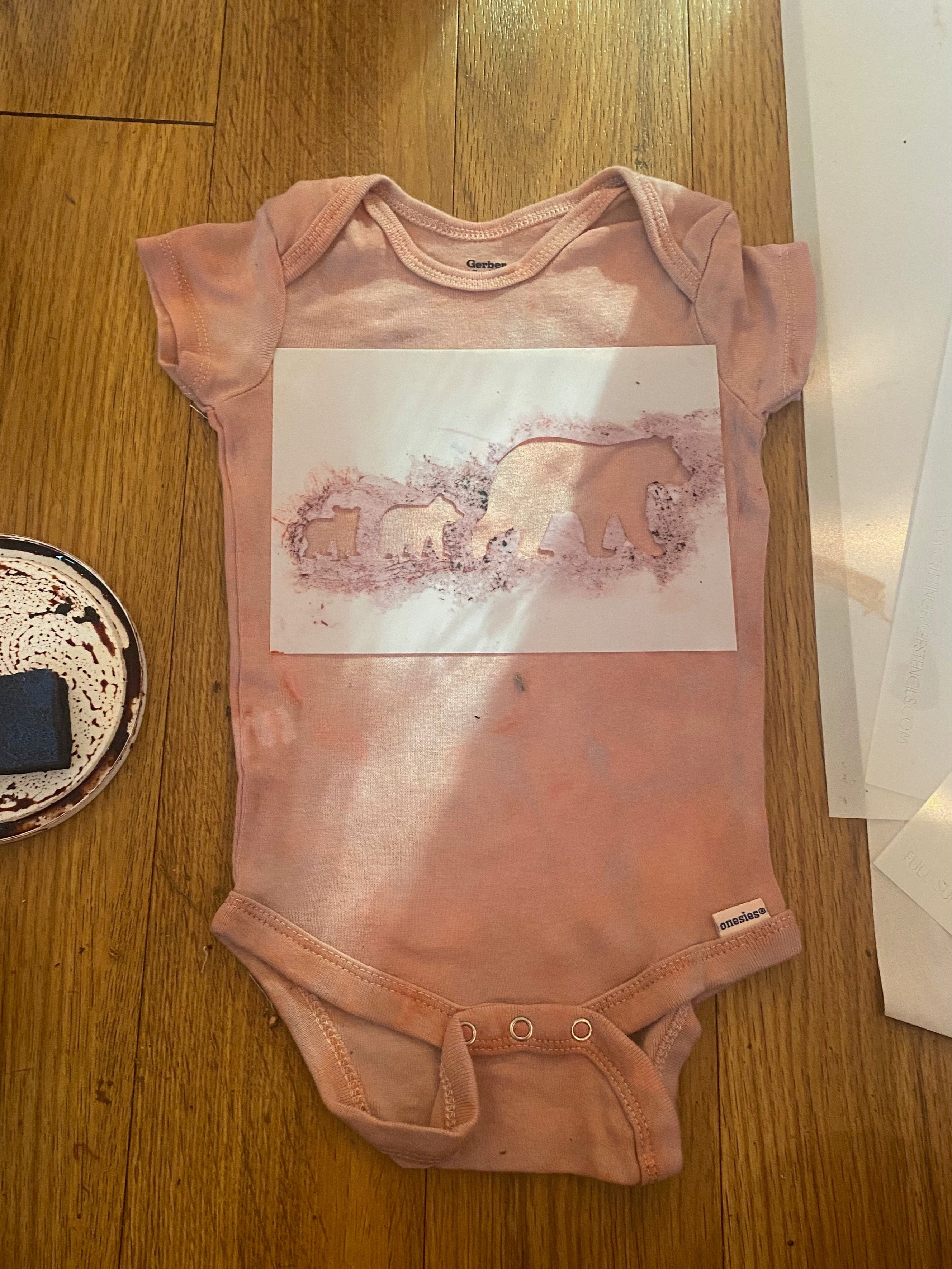 Pink baby onesie with a bear stencil on a wooden surface