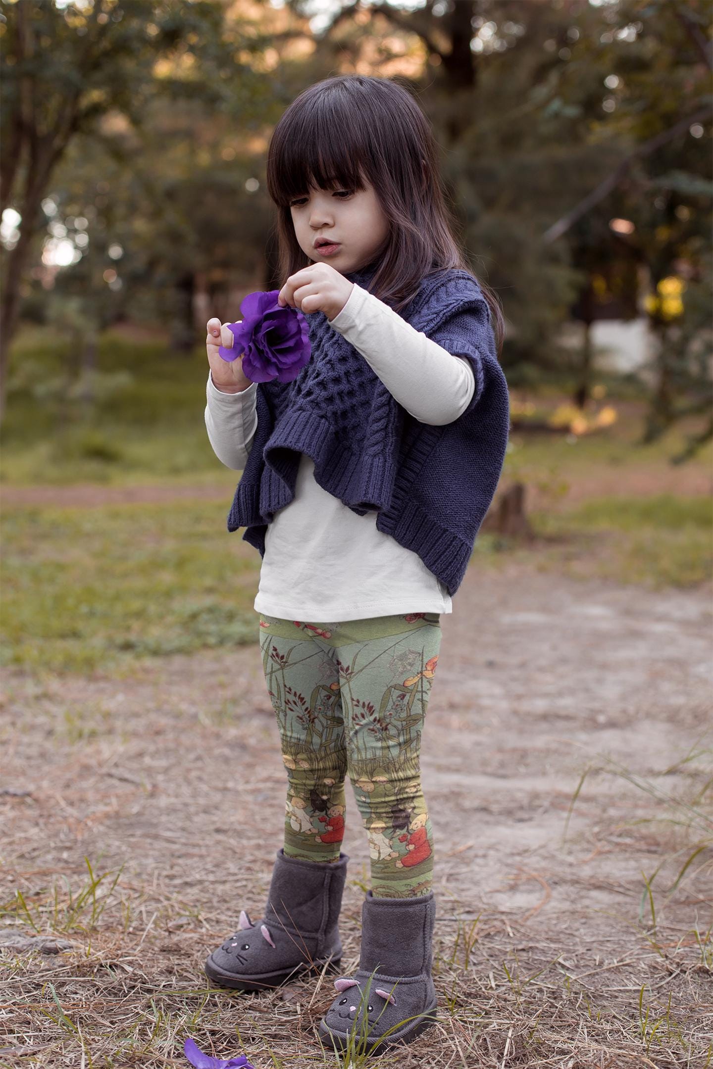 Little girl wearing green and blue illustrated leggings from Elsa beskows the root children. the leggings have images of little flower children in simple clothes and beautiful flowers. they are mostly teal green with some teal blue