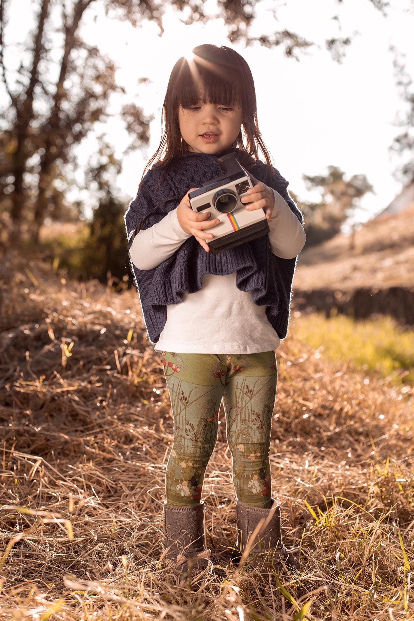 Little girl wearing green and blue illustrated leggings from Elsa beskows the root children. the leggings have images of little flower children in simple clothes and beautiful flowers. they are mostly teal green with some teal blue