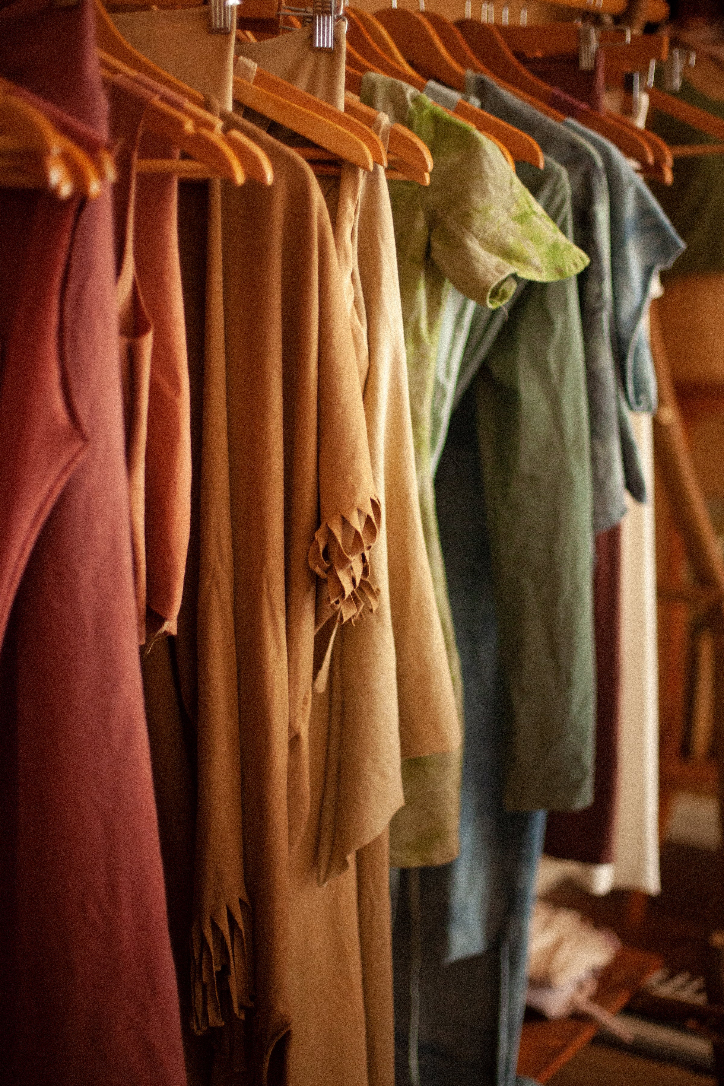 naturally dyed clothing in rainbow shades on wooden hangers on a rack