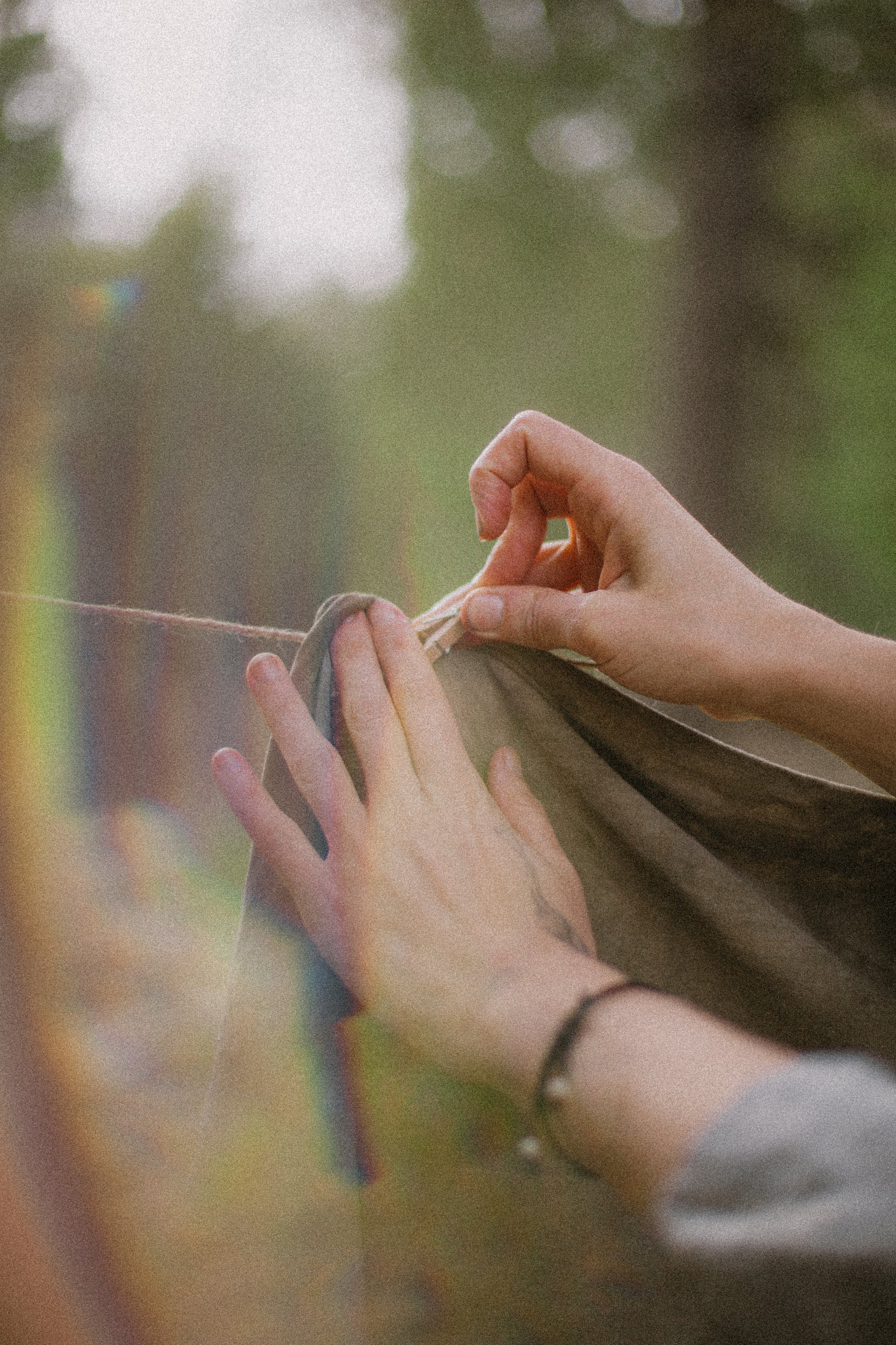 hands hanging fabric on a clothing line with rainbow light filtering in through the edges