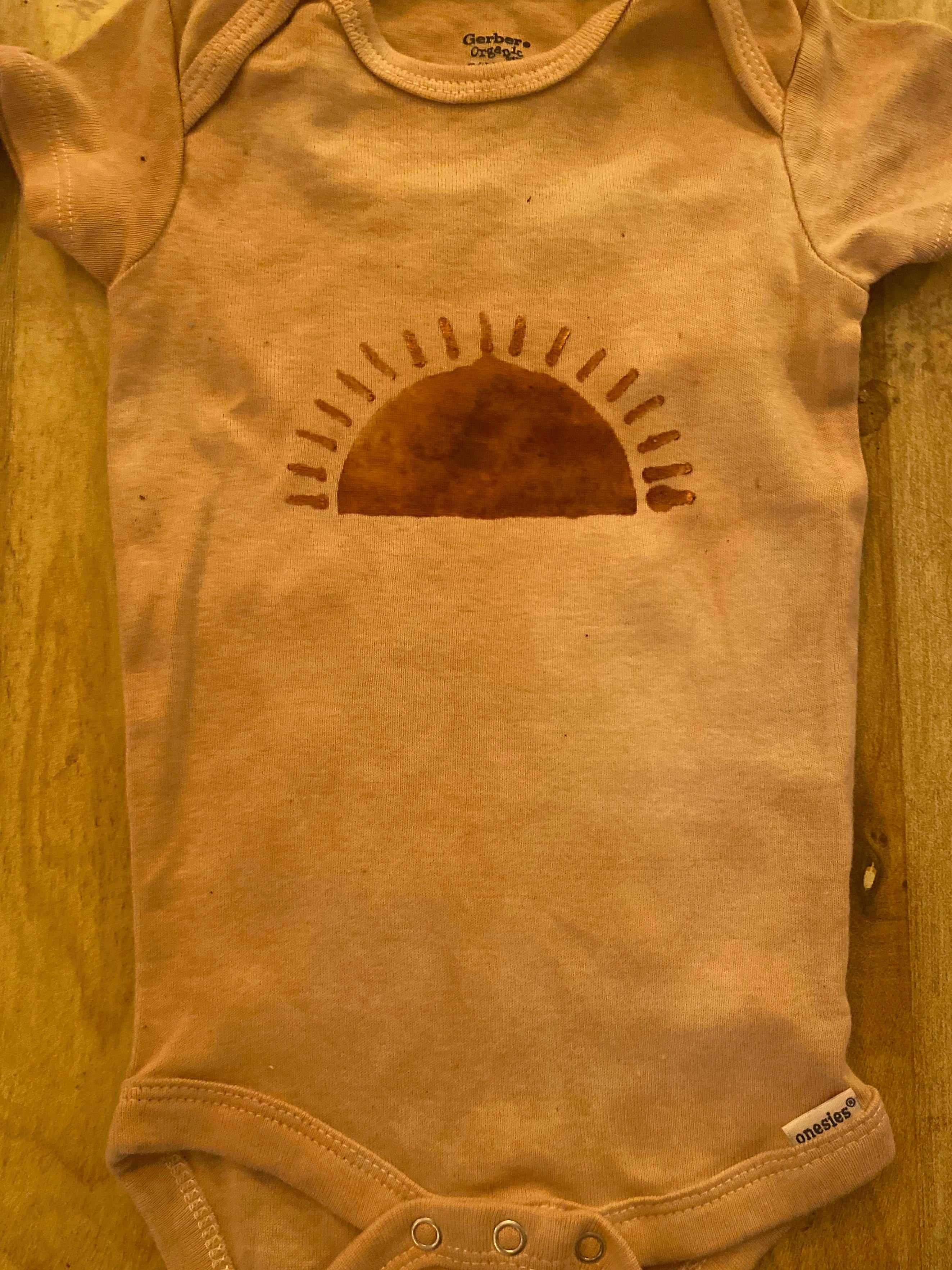 pink Brown baby onesie with a sun design on a wooden surface