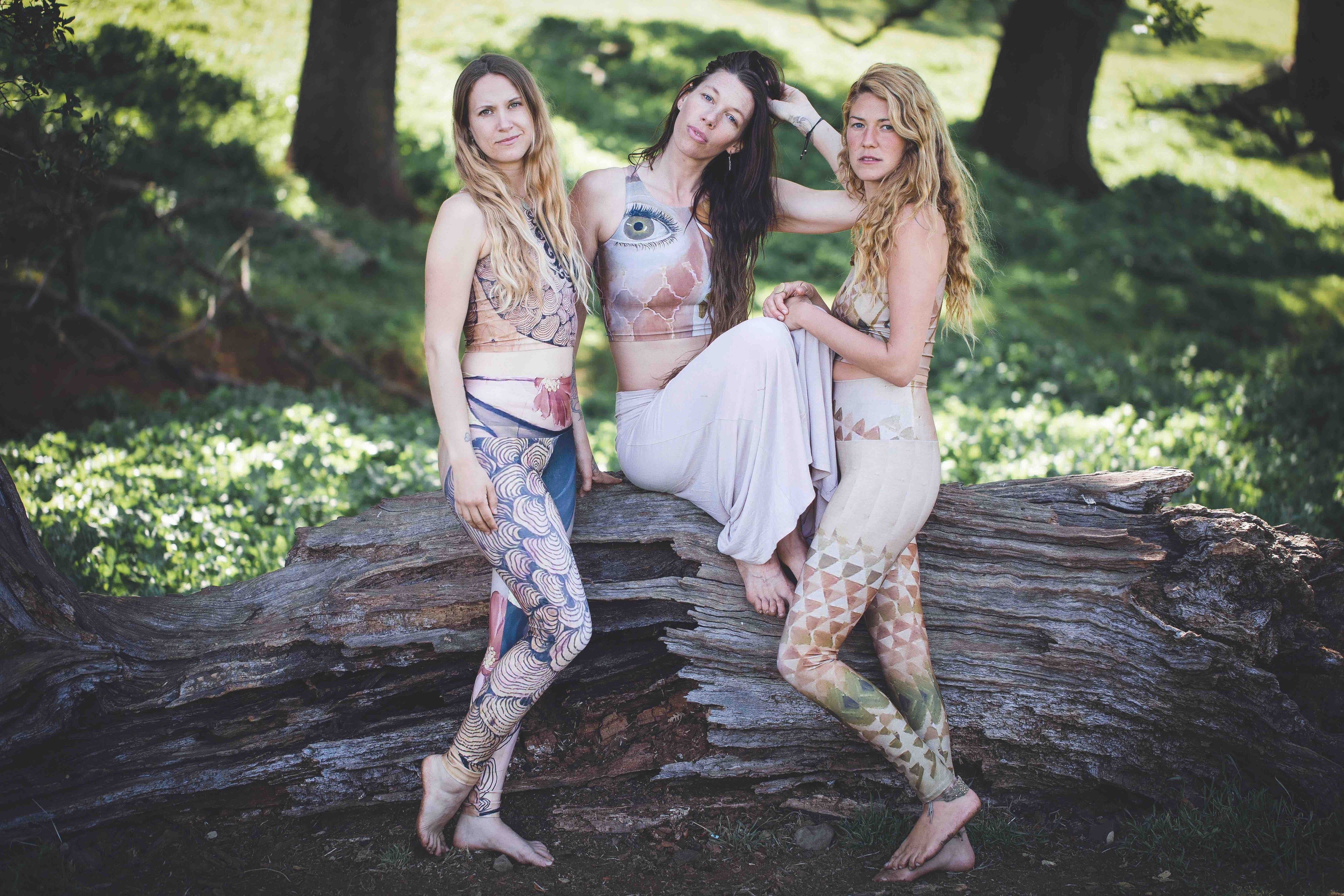 3 women wearing Yoga leggings with a woman face and reishi mushroom black lines painted on reclaimed wood with a gold earring and a red flower