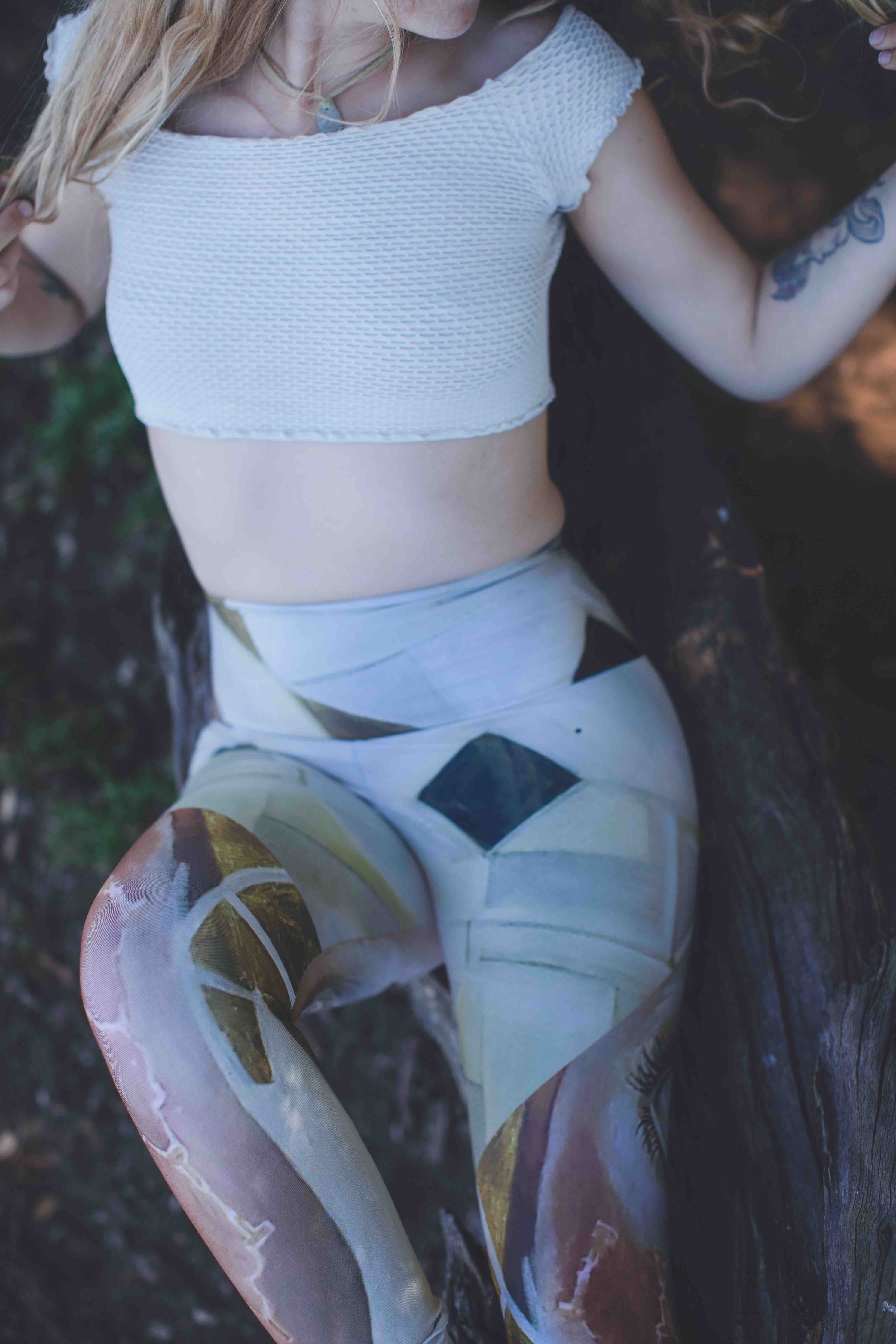 woman wearing Yoga leggings in shades of white cream and gold with pink accents and geometric gold shapes  and a white top