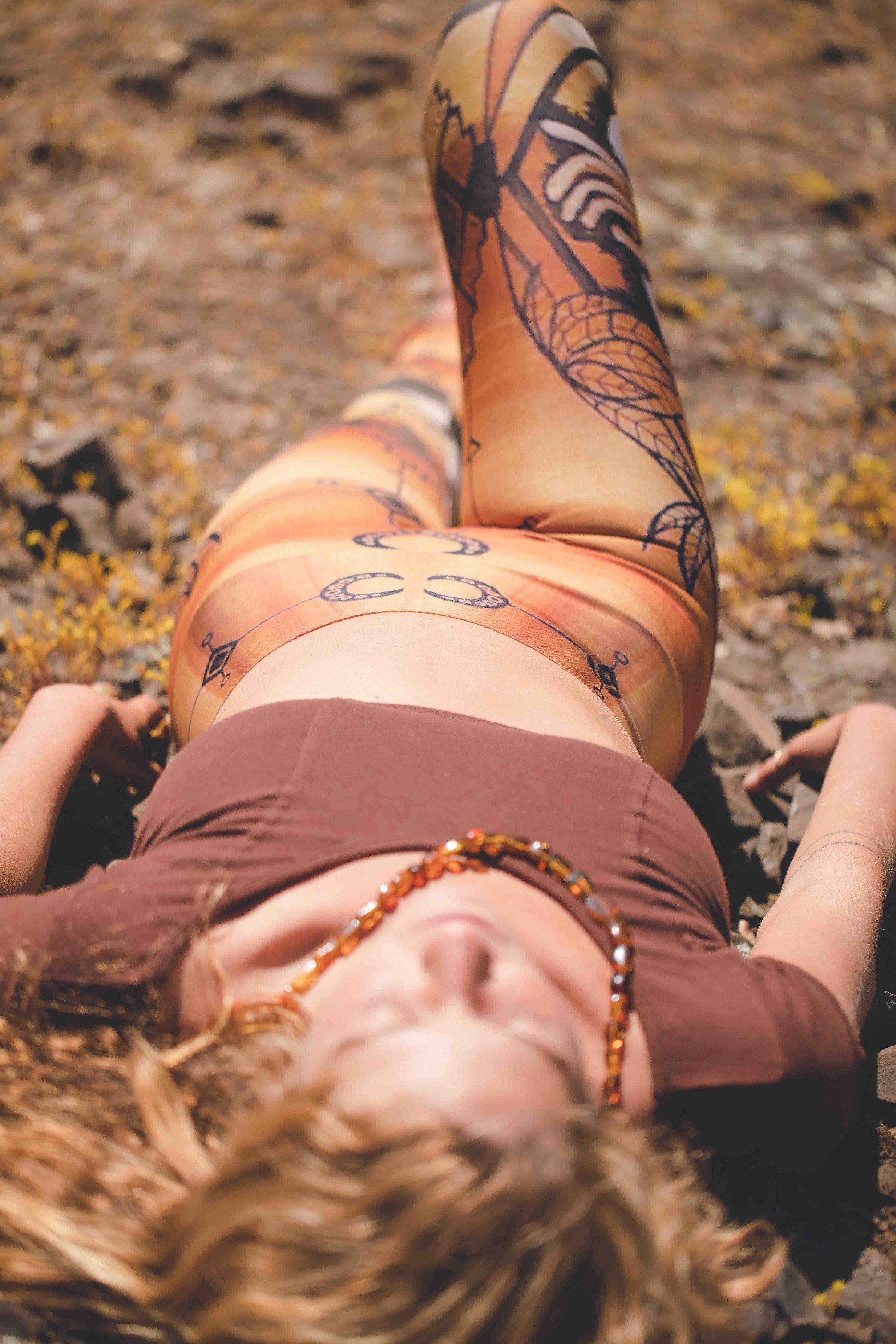 A person lounging on a rocky surface wearing leggings with a floral and crescent moon design in golden brown and rust colors.