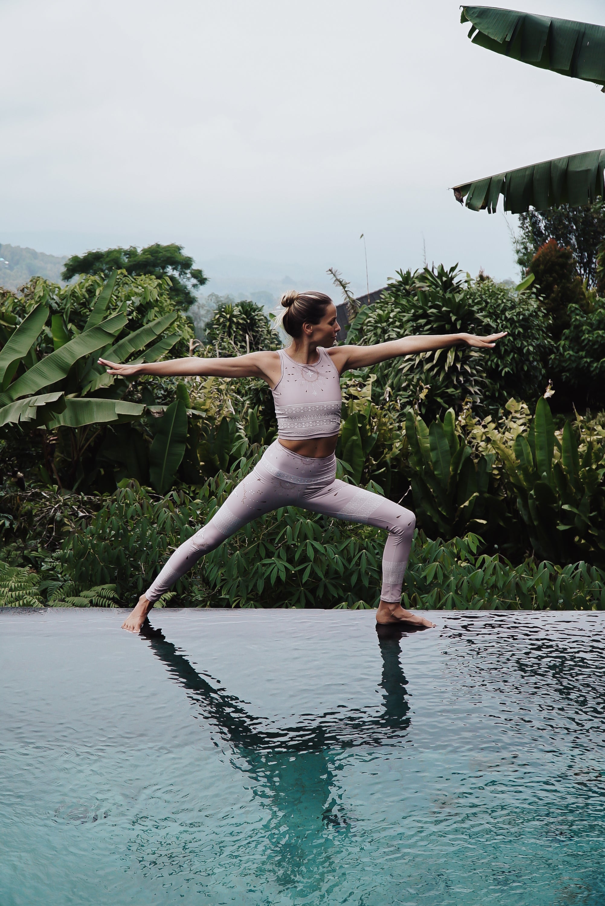 woman doing yoga in the warrior asana on the edge of an infinity pool in the jungle
