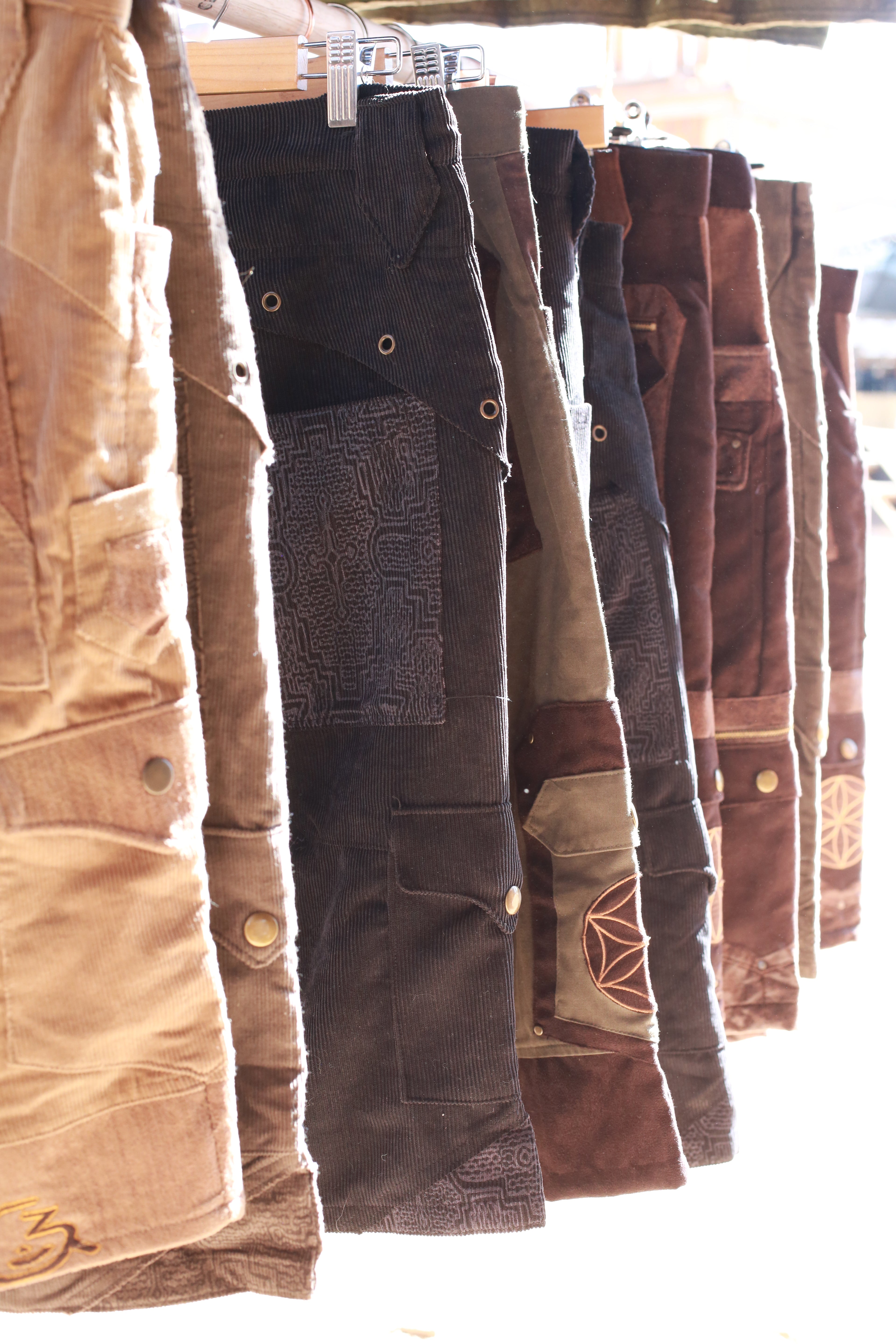 mens cargo shorts in unique fabrics and prints hanging on a wooden rack in shades of beige brown and black