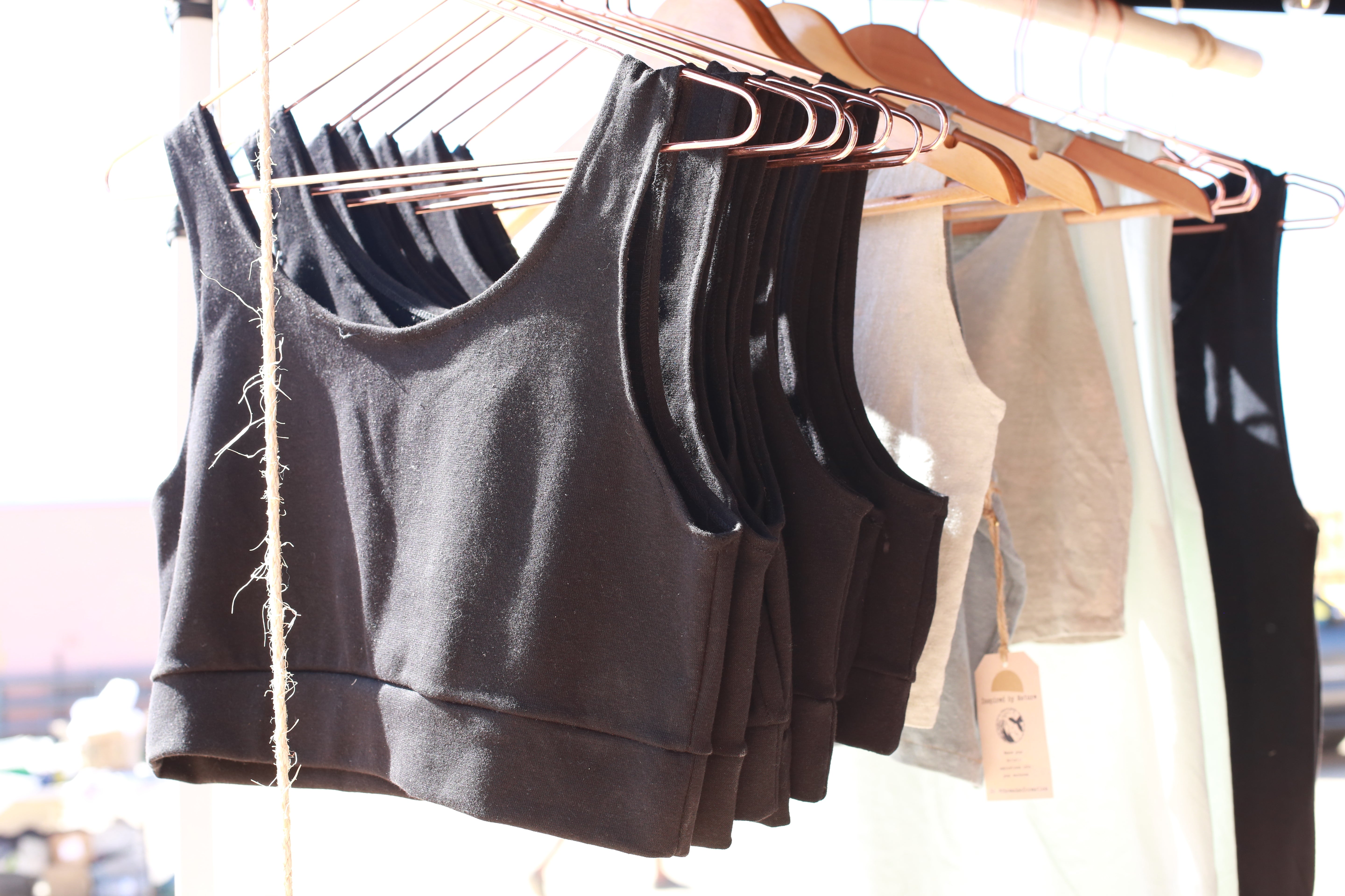 rack of black bra tops hanging in the sun on rose gold and wooden hangers