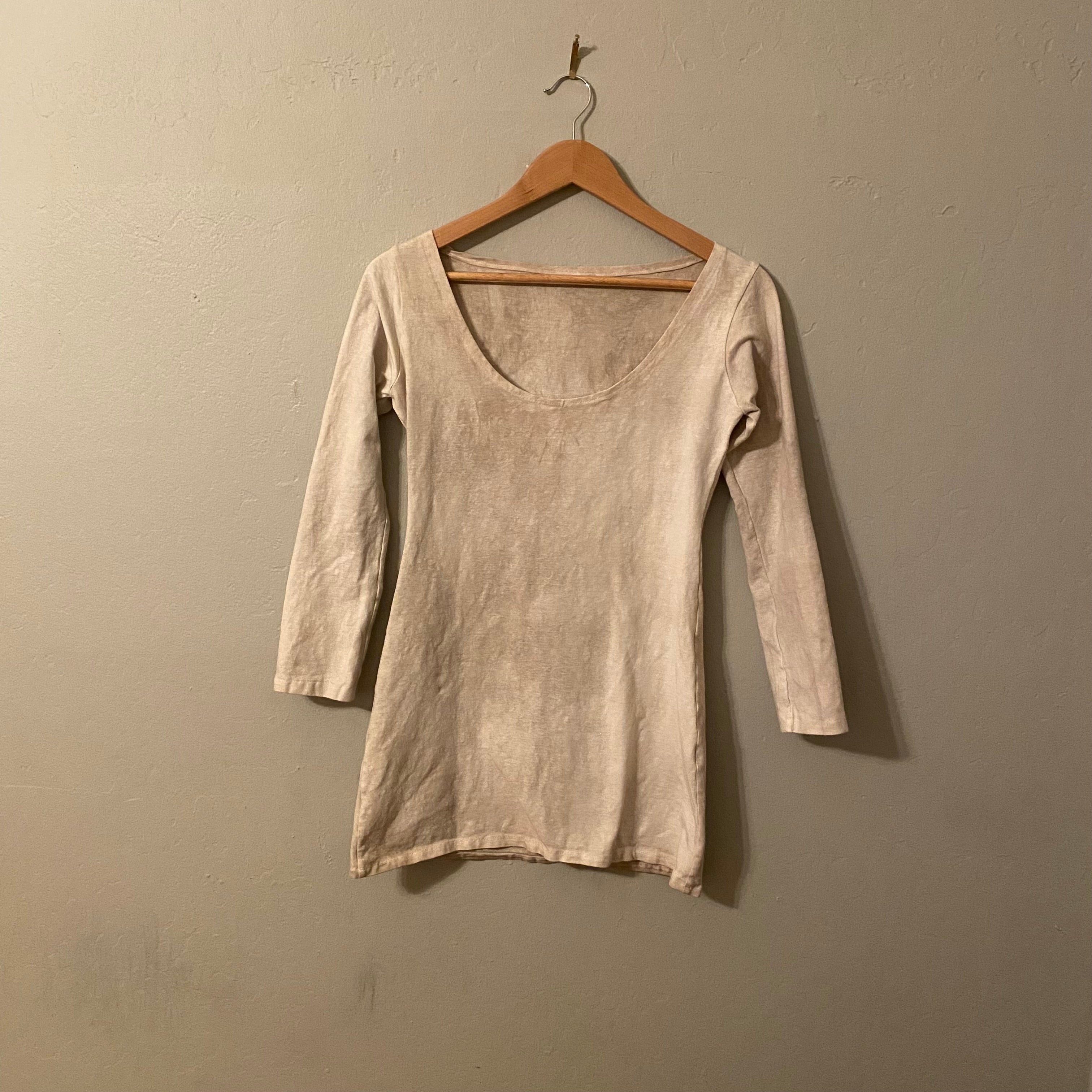 cream/white tunic dress hanging in a wooden hanger against a plain wall
