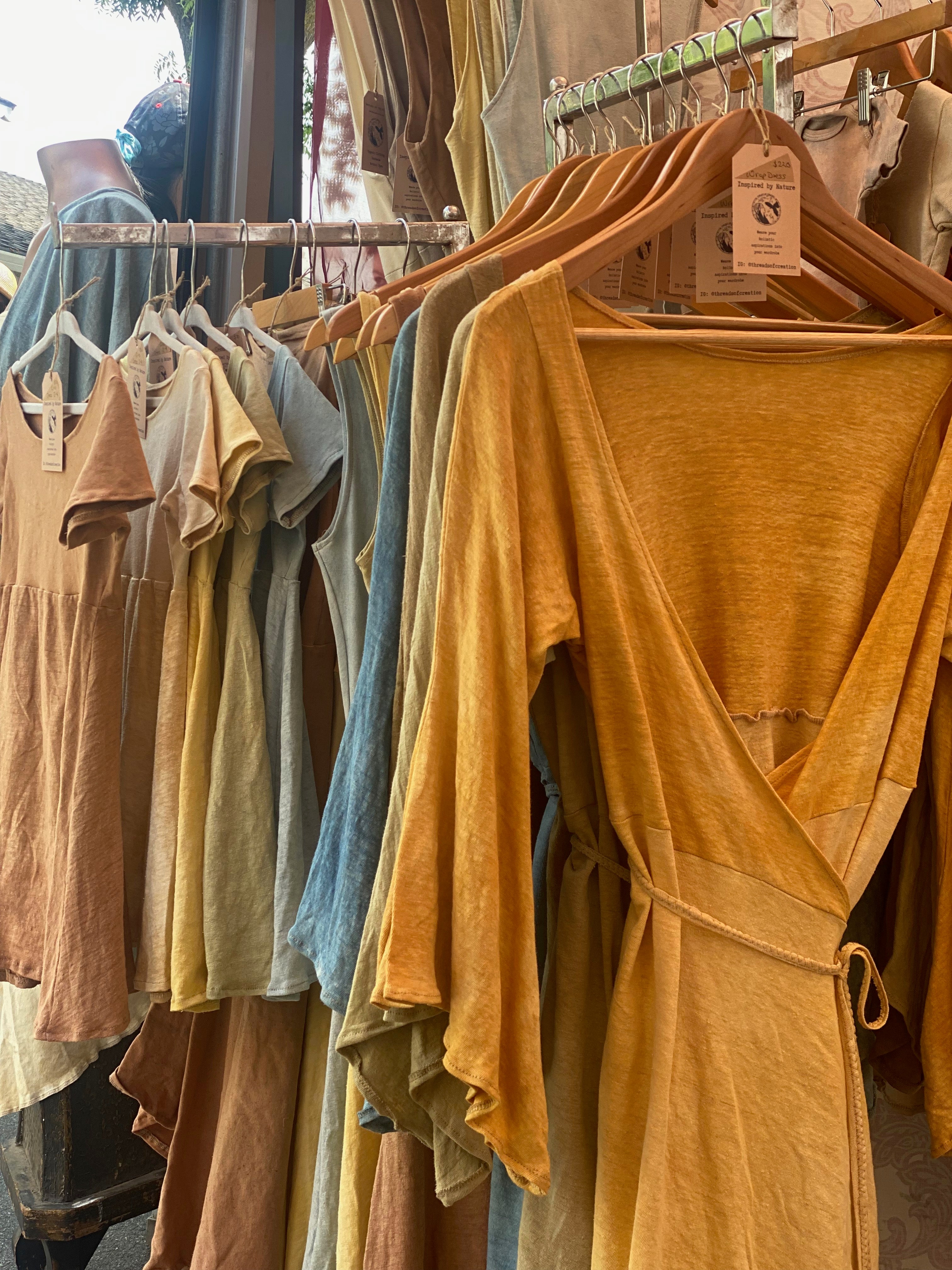 front view of rack of wrap dresses starting with bright yellow on wooden hangers and matching little girls dresses next to them