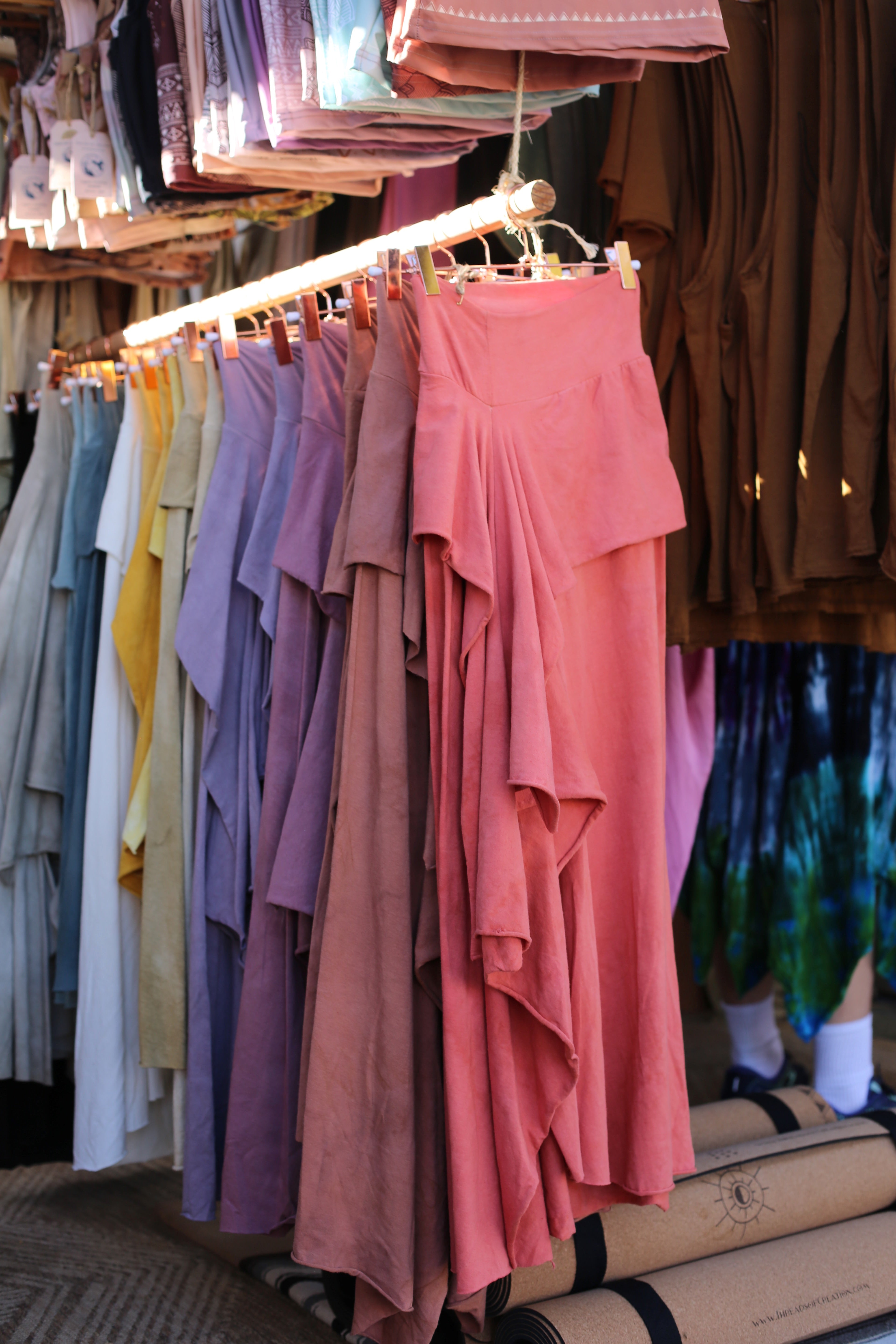 front view of a rack of skirts in a range of colors from red throhgh brown and purples and yellows hanging on a wooden rack in a shop setting