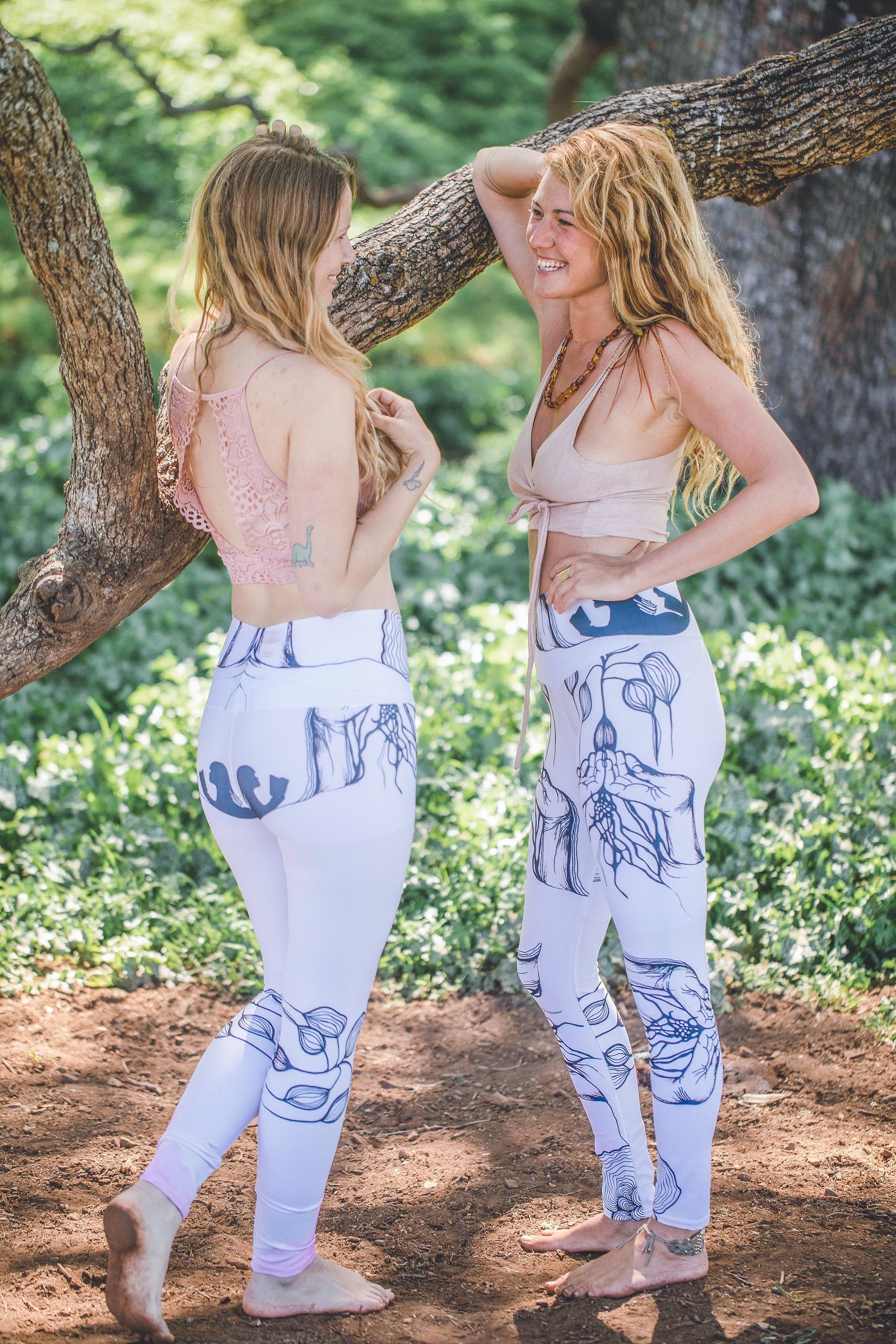 2 models with blonde wavy hair wearing black and white leggings and pink tops standing outside next to a tree