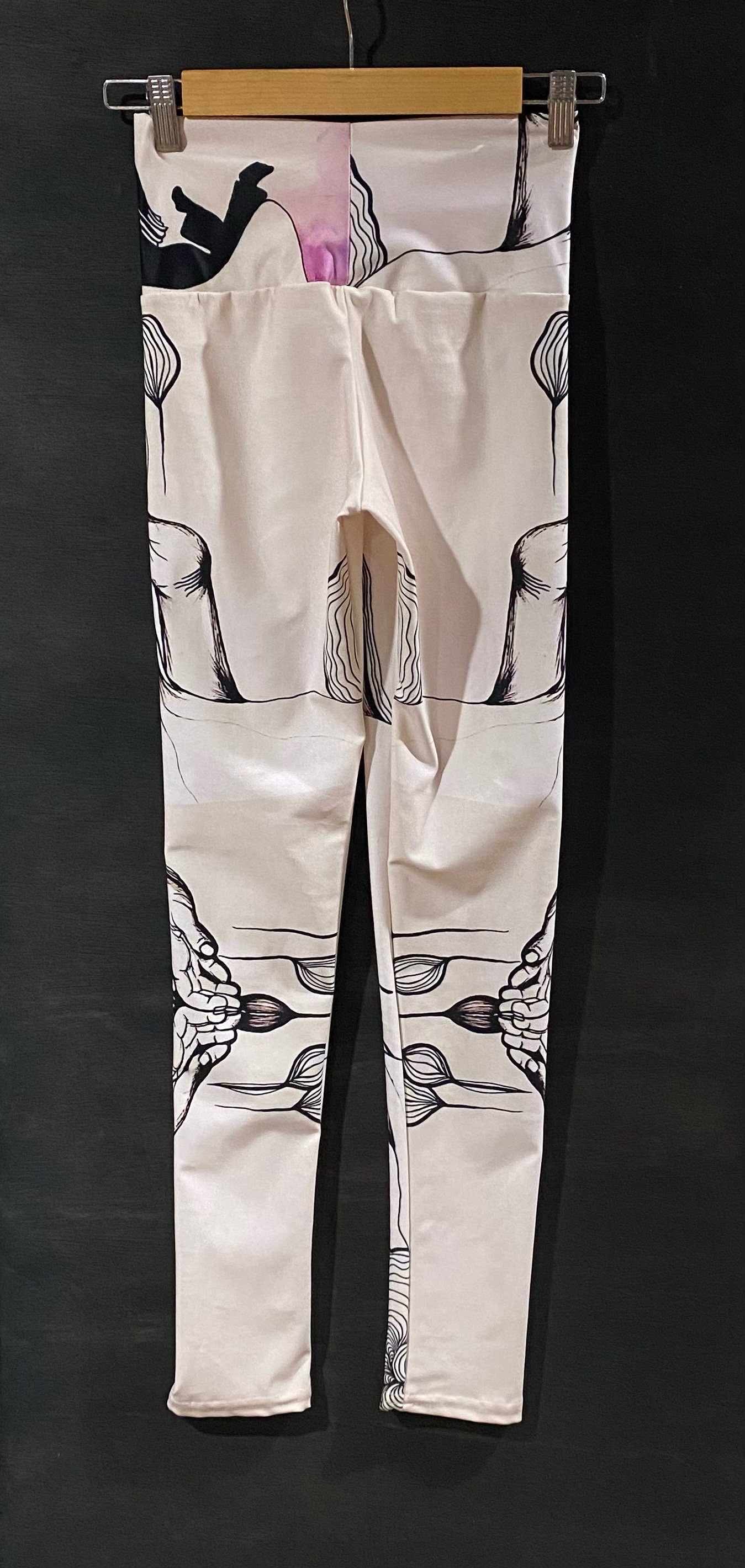 black and white leggings with seed design on a wooden hanger against a dark background
