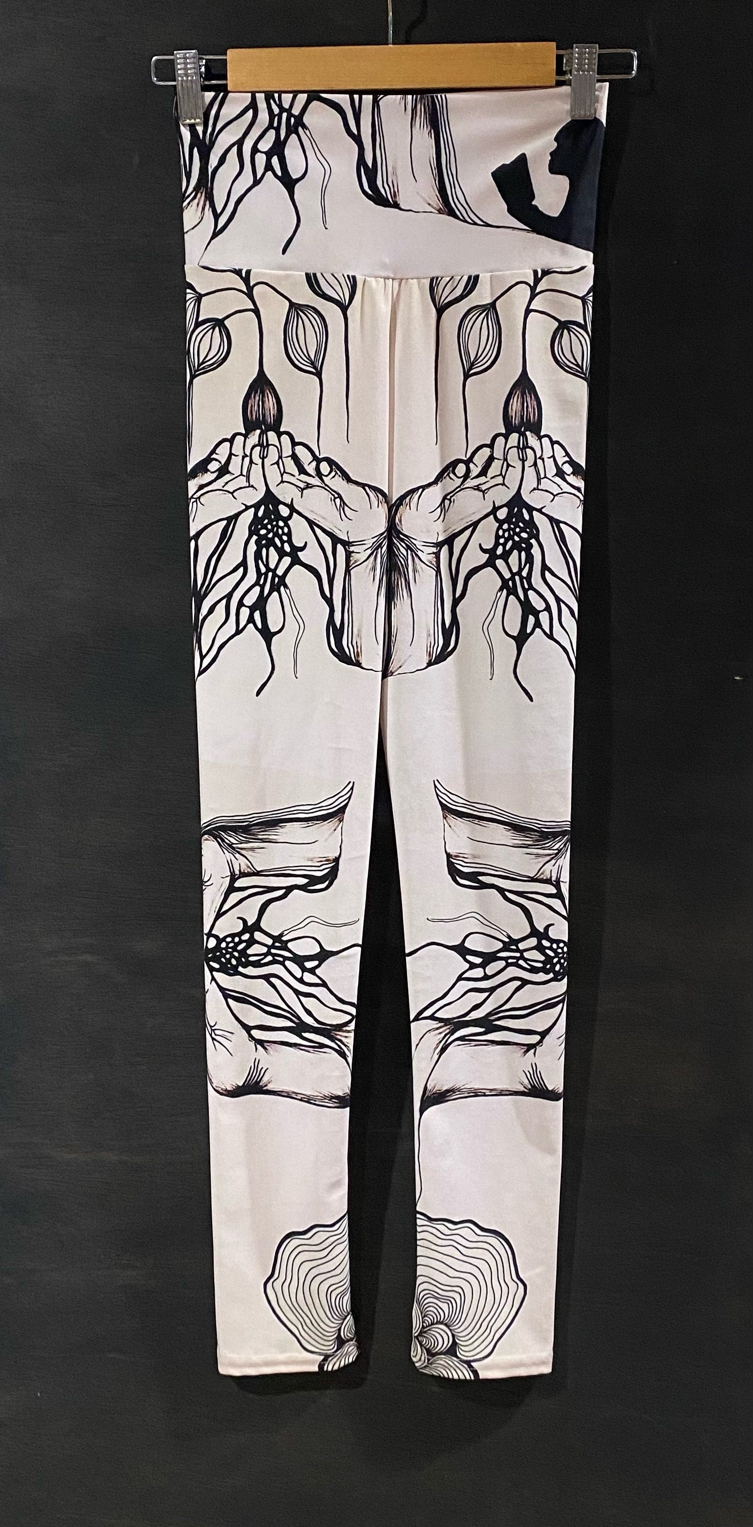 black and white leggings with seed design on a wooden hanger against a dark background