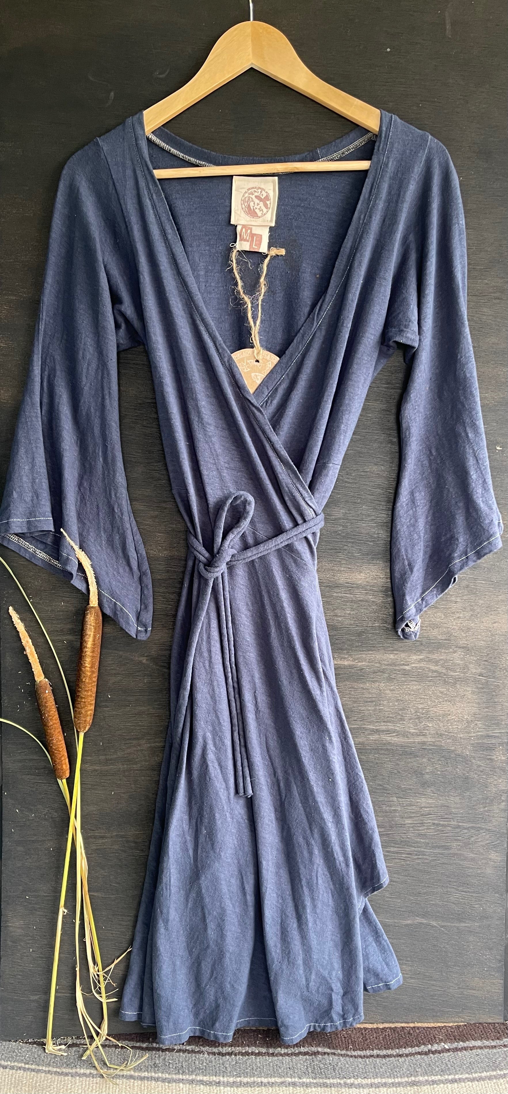 A blue and black wrap dress with bell sleeves, displayed on a hanger against a wooden background with a tag showing 'Raven'.