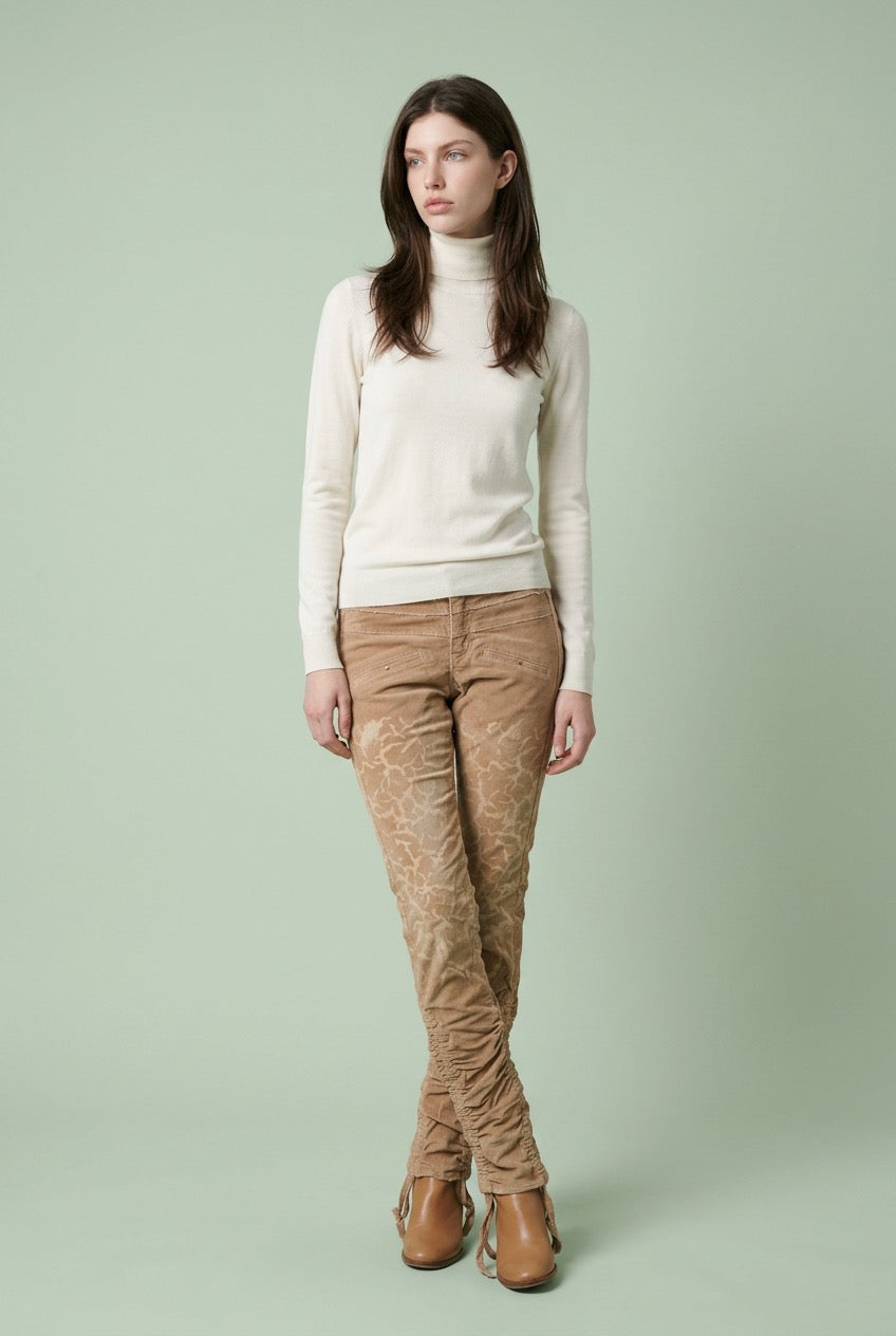Woman wearing a cream sweater and brown patterned corduroypants on a light green background