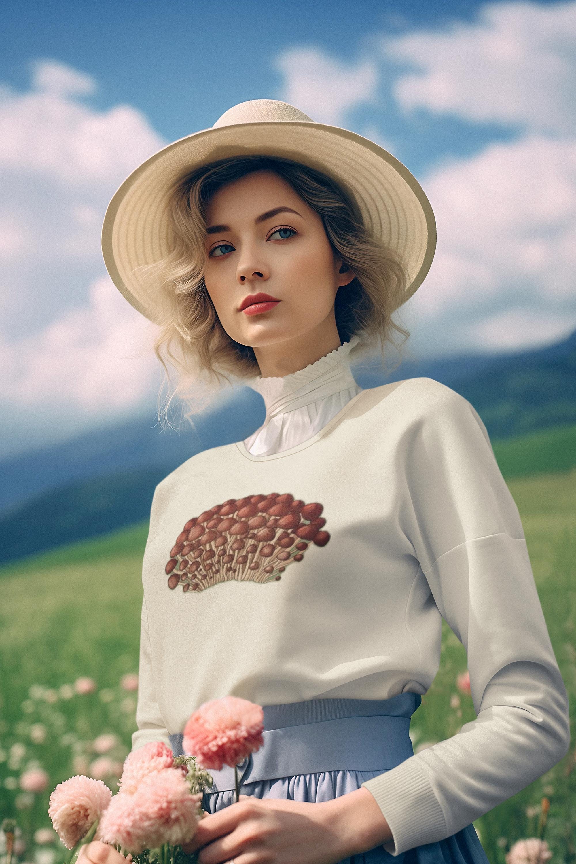 Beautiful woman with blonde short wavey hair in a flower meadow holding pink dahlia flowers wearing a crewneck sweatshirt in cream with tiny little red and beige mushrooms