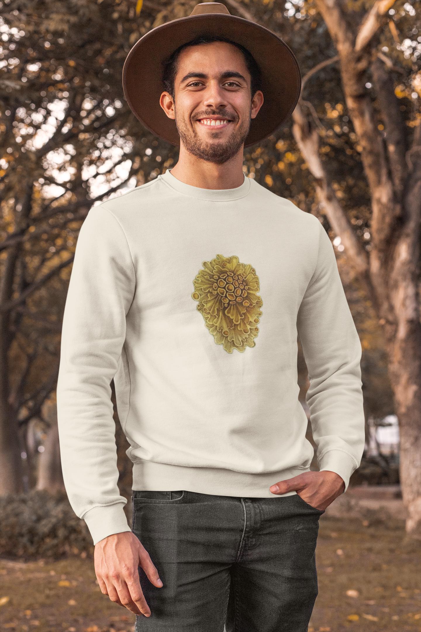 beautiful man standing in a tree park. he has long brown wavey hair and he is wearing a cream crewneck sweater with yellow wavey mushrooms printed on it