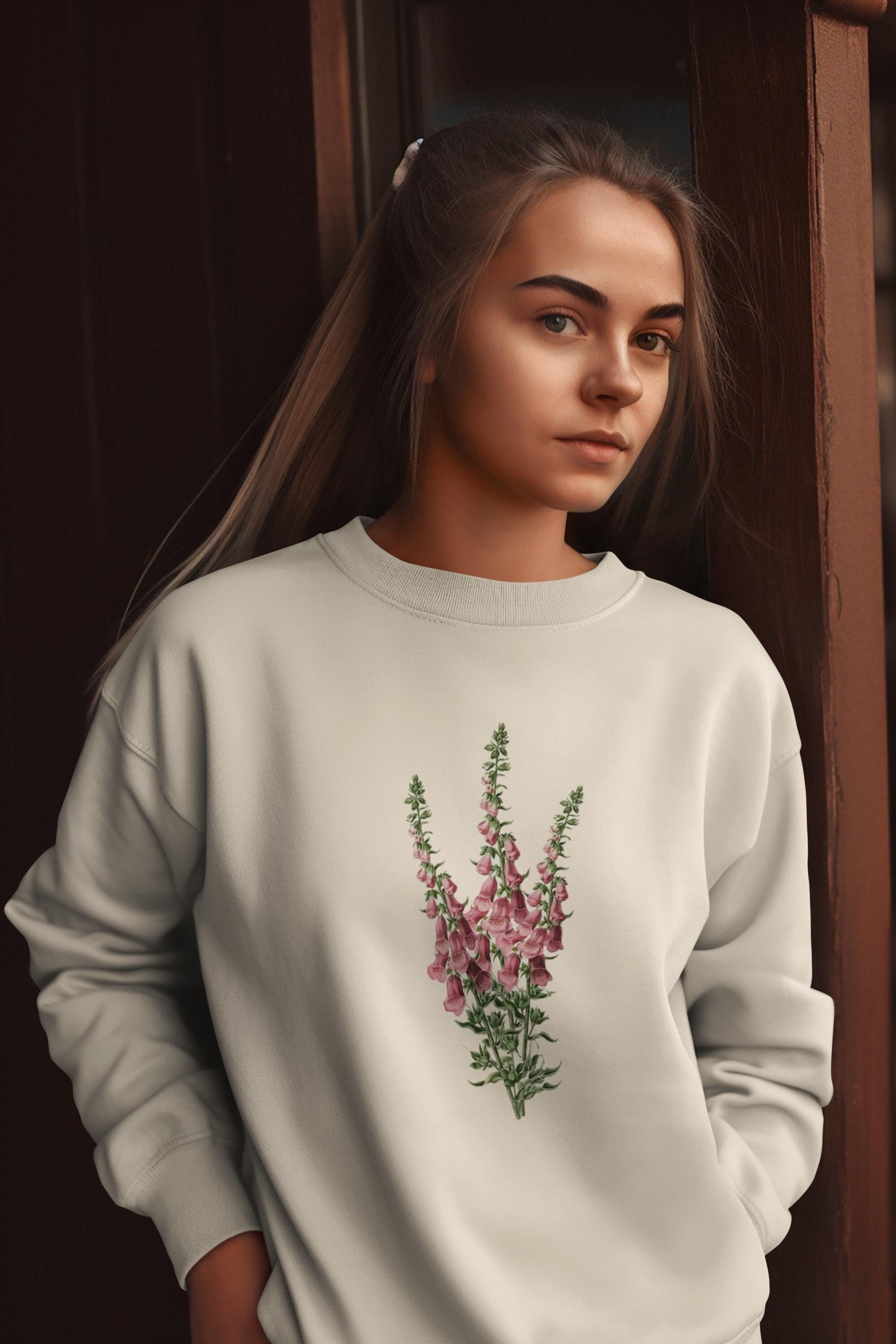 Young woman with blonde ponytail standing wearing a cream crewneck sweatshirt with a foxglove flower print on it