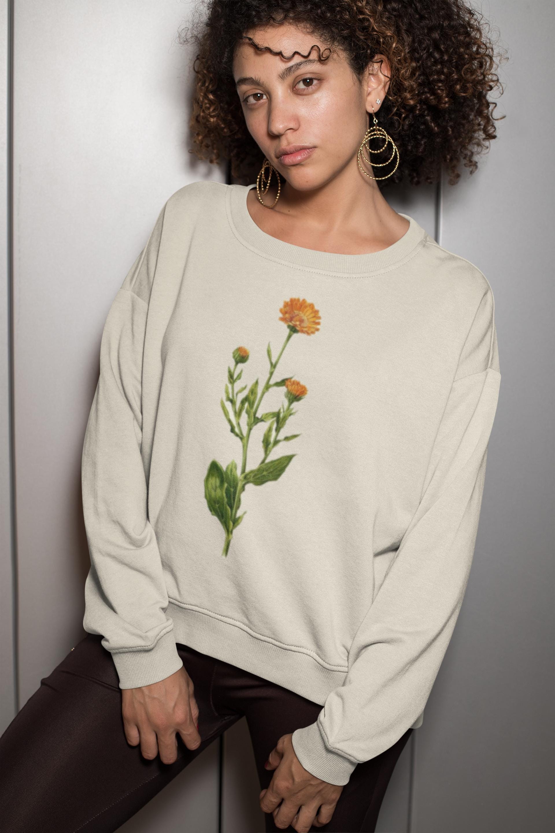 woman swearing a cream colored crewneck sweatshirt with a calendula flower printed on it