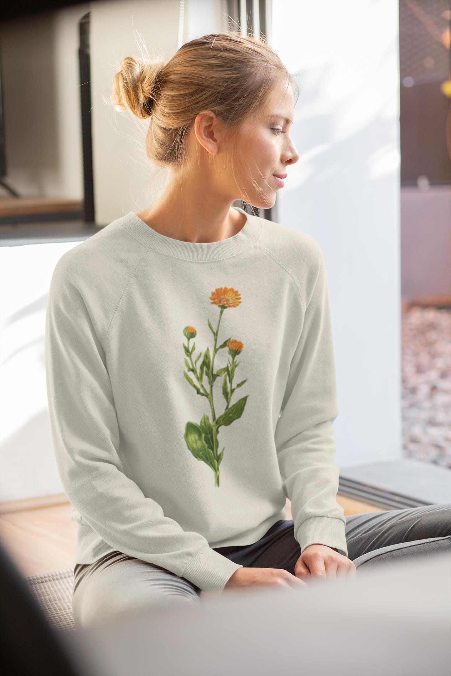 woman swearing a cream colored crewneck sweatshirt with a calendula flower printed on it