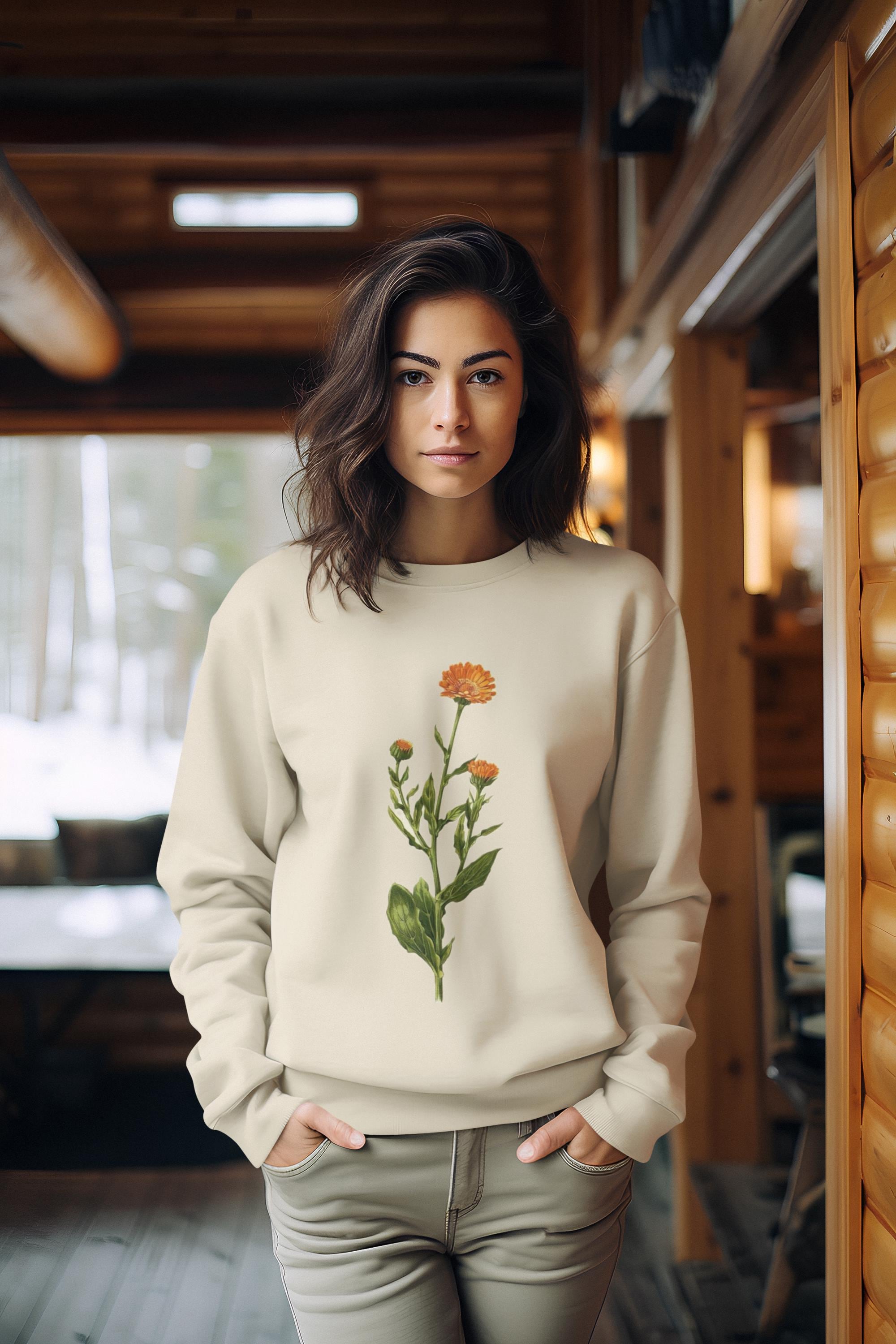 woman swearing a cream colored crewneck sweatshirt with a calendula flower printed on it