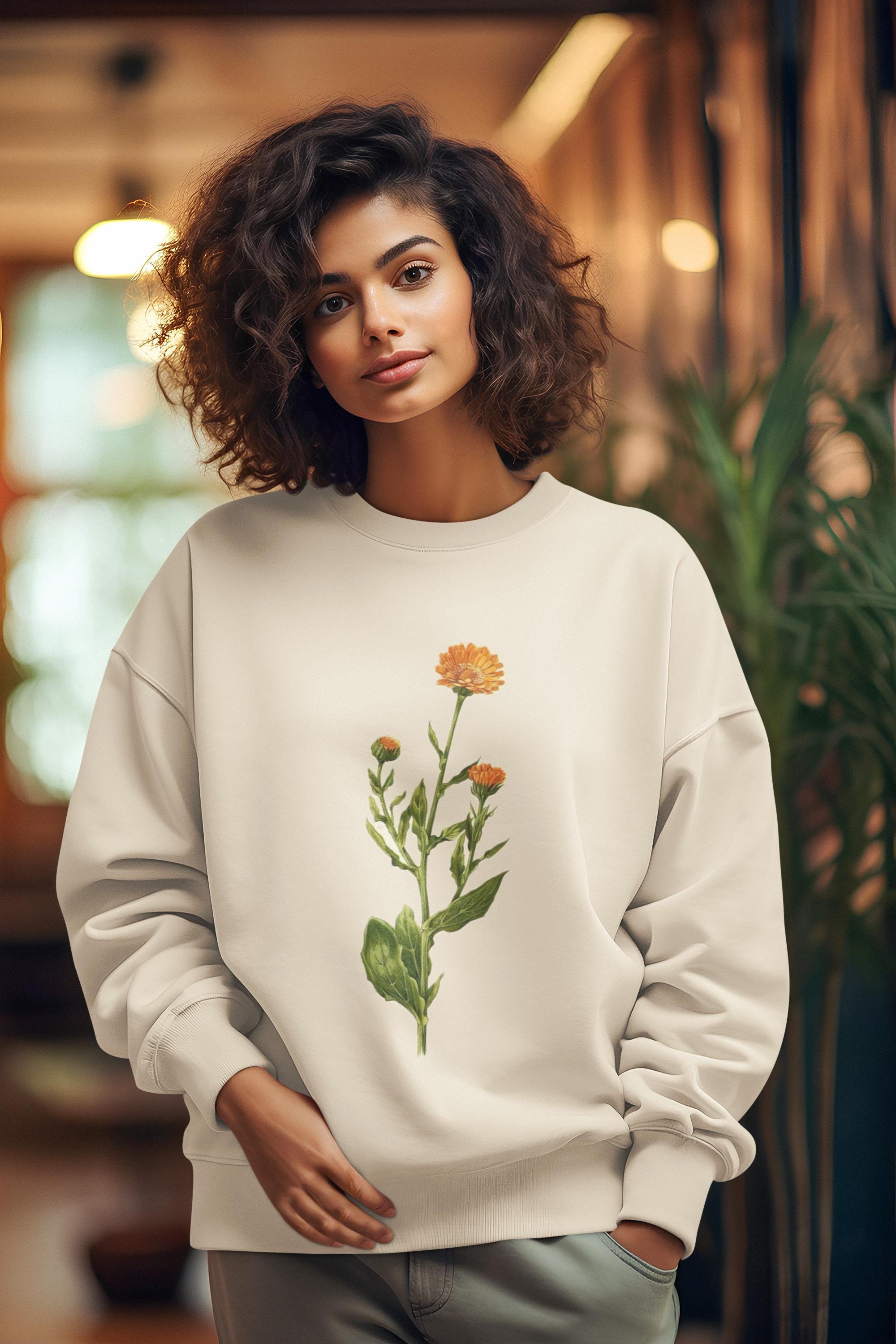 woman swearing a cream colored crewneck sweatshirt with a calendula flower printed on it