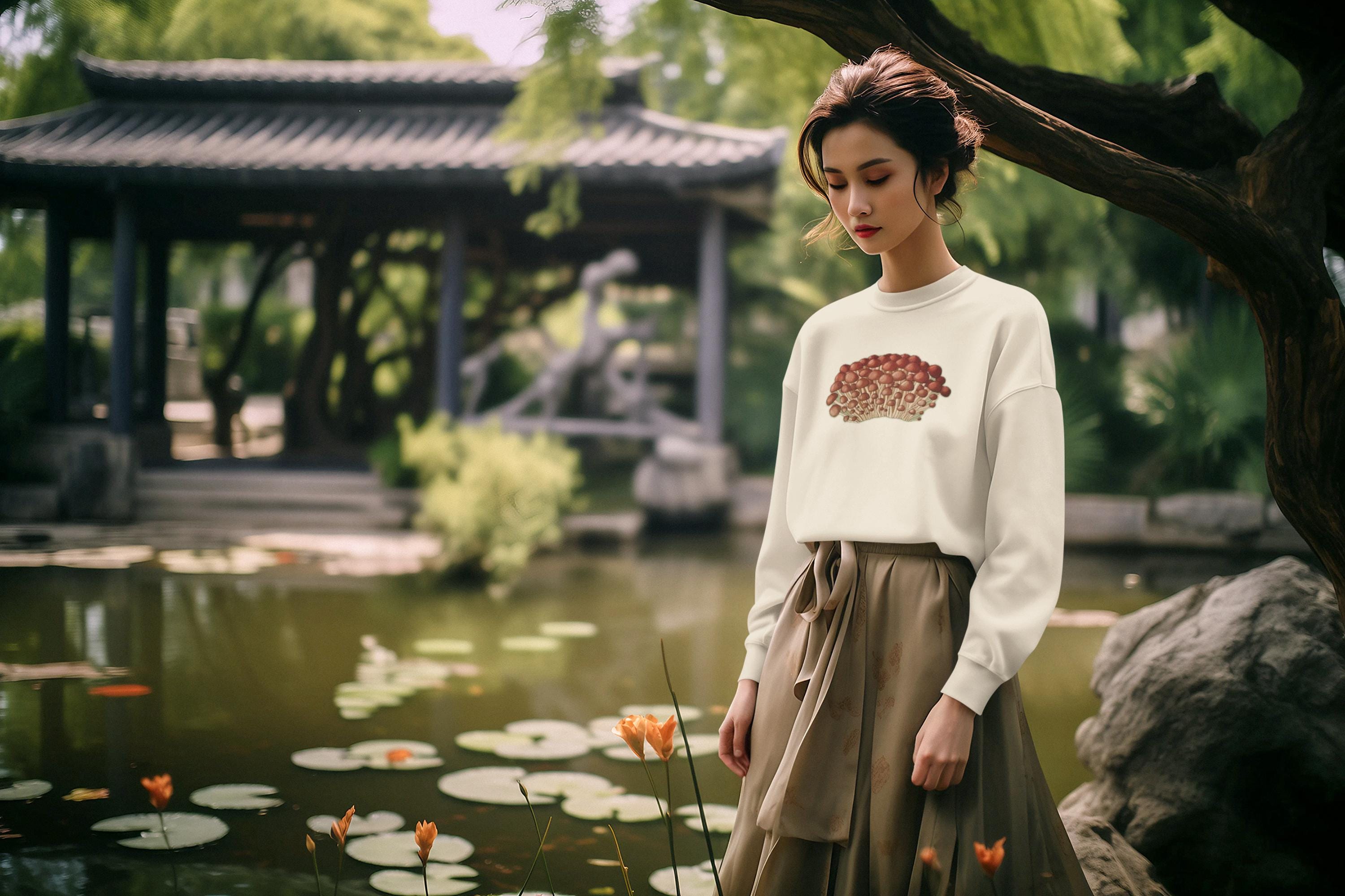 Beautiful woman with brown mid length hair tied up in a tranquil peaceful garden next to a pond with lily pads and flowers wearing a crewneck sweatshirt in cream with tiny little red and beige mushrooms