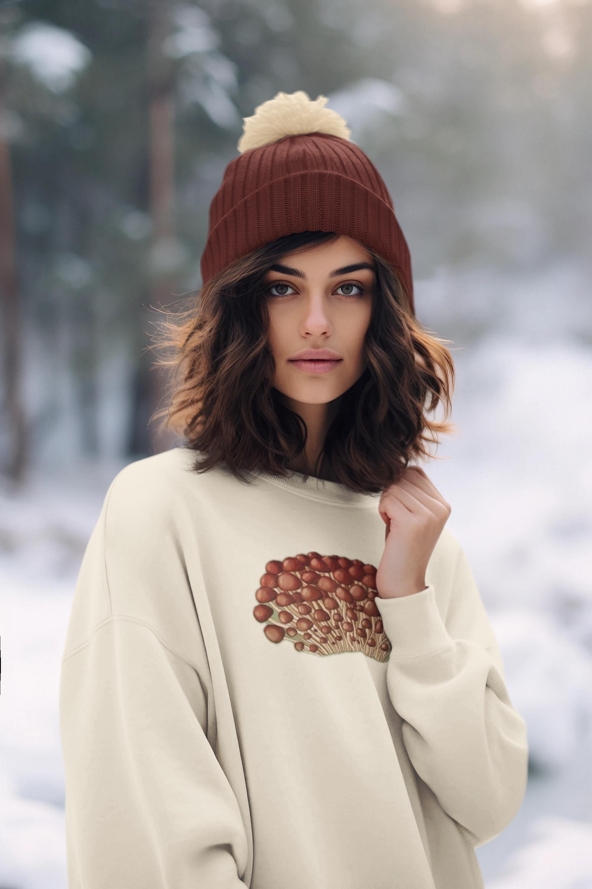 Beautiful woman with brown mid length wavey hair in a snowy forest wearing a crewneck sweatshirt in cream with tiny little red and beige mushrooms and a matching red and cream hat