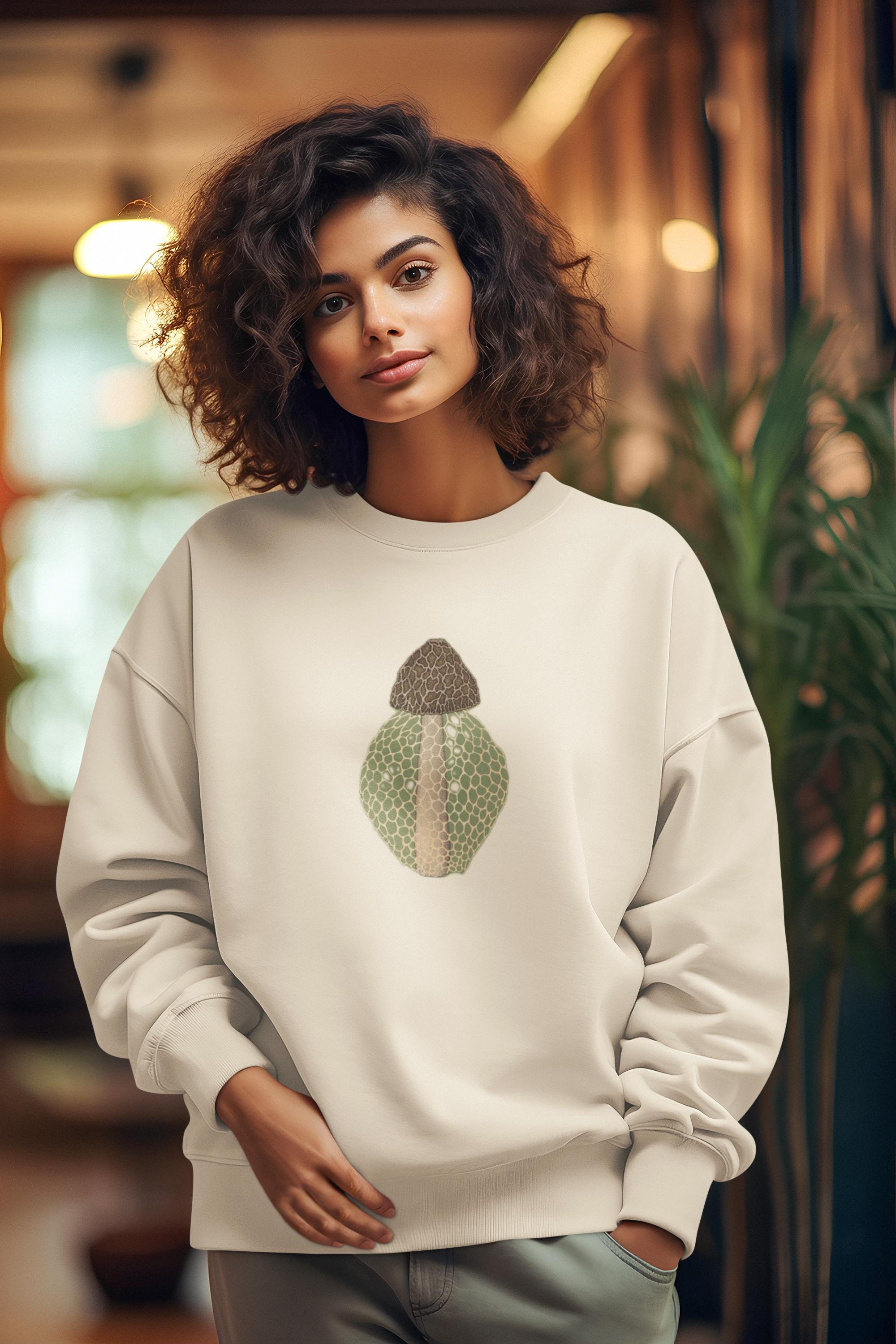 Beautiful woman with dark curly hair standing in a restaurant wearing a crew neck sweatshirt with a brown beige and green morel on it