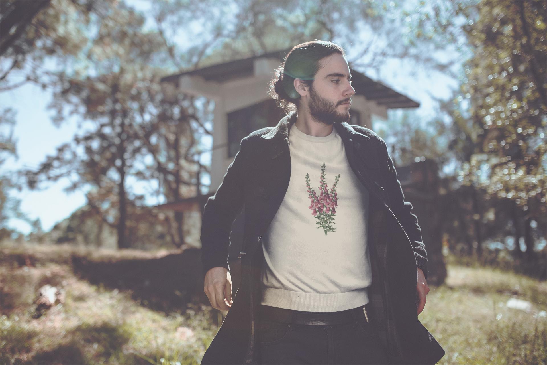 Young man with dark hair in a ponytail standing wearing a cream crewneck sweatshirt with a foxglove flower print on it