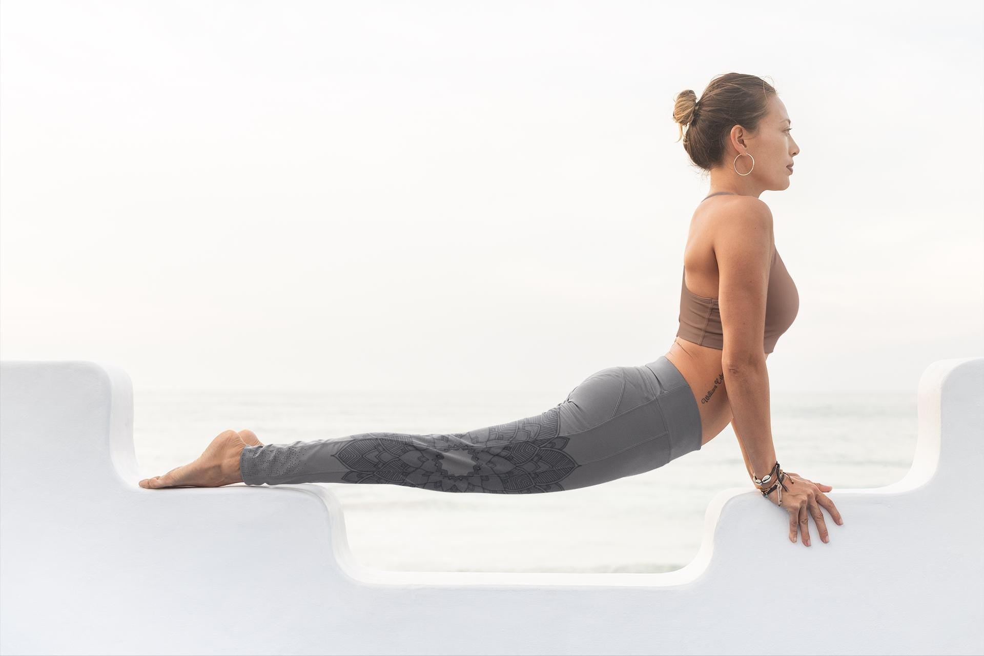 woman doing yoga and wearing yoga leggings in shades of heather grey and black with a lotus lace design on them