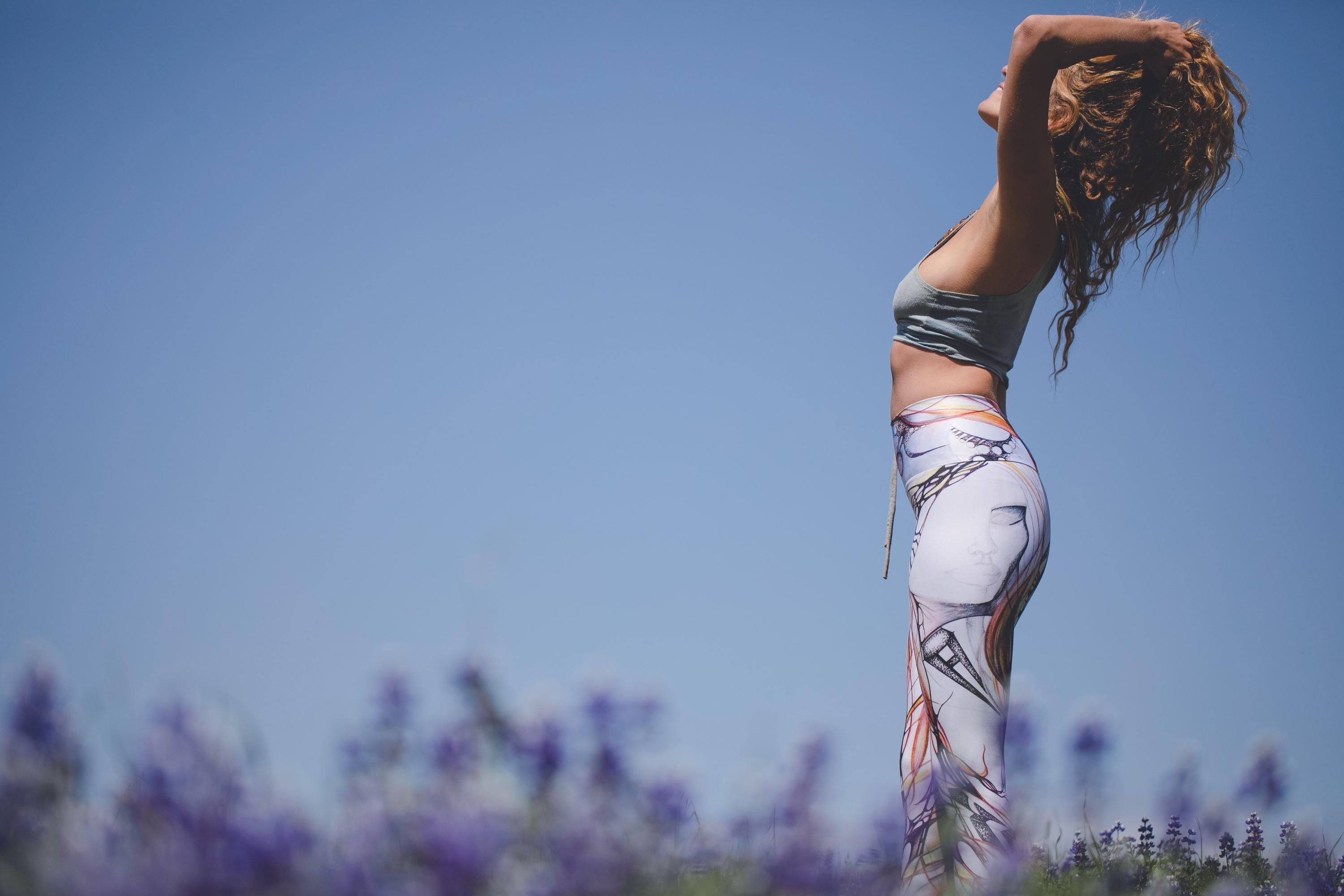 woman wearing Yoga leggings with black and white lines and designs in organic shapes with shades of blue and red in a field of flowers with a blue sky