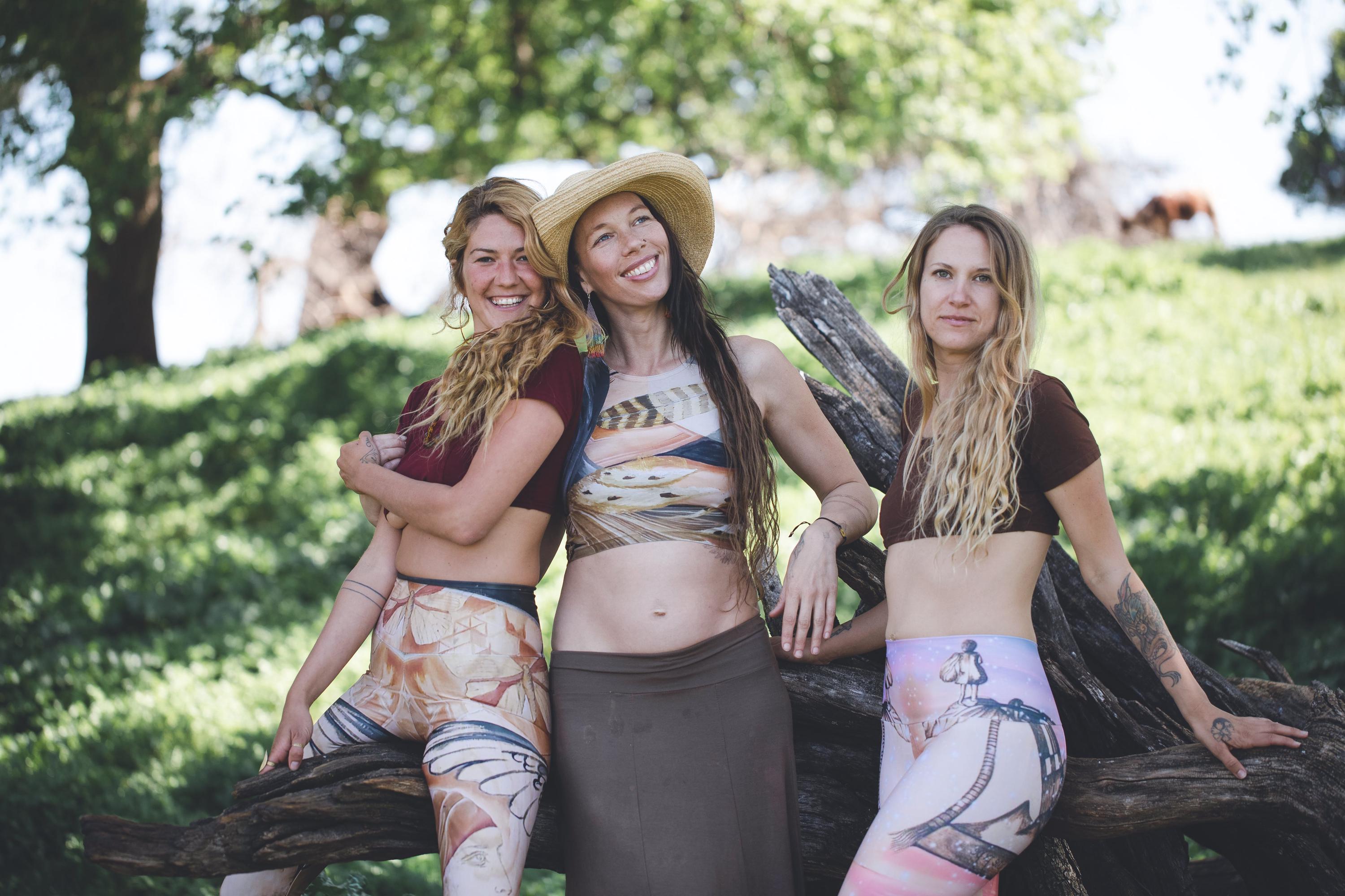 3 women sitting on a tree wearing artistic yoga sets in earthy shades