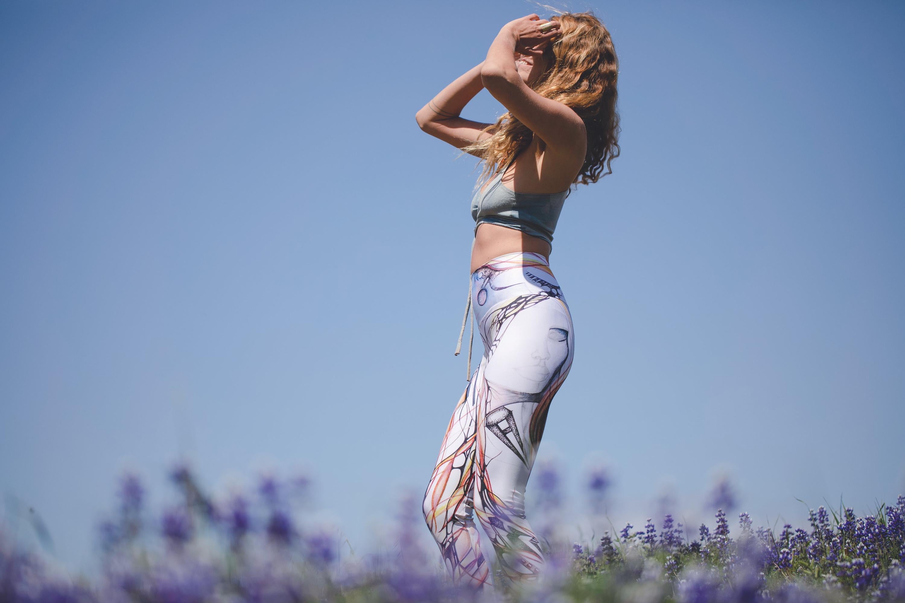 woman wearing Yoga leggings with black and white lines and designs in organic shapes with shades of blue and red in a field of flowers and a blue sky