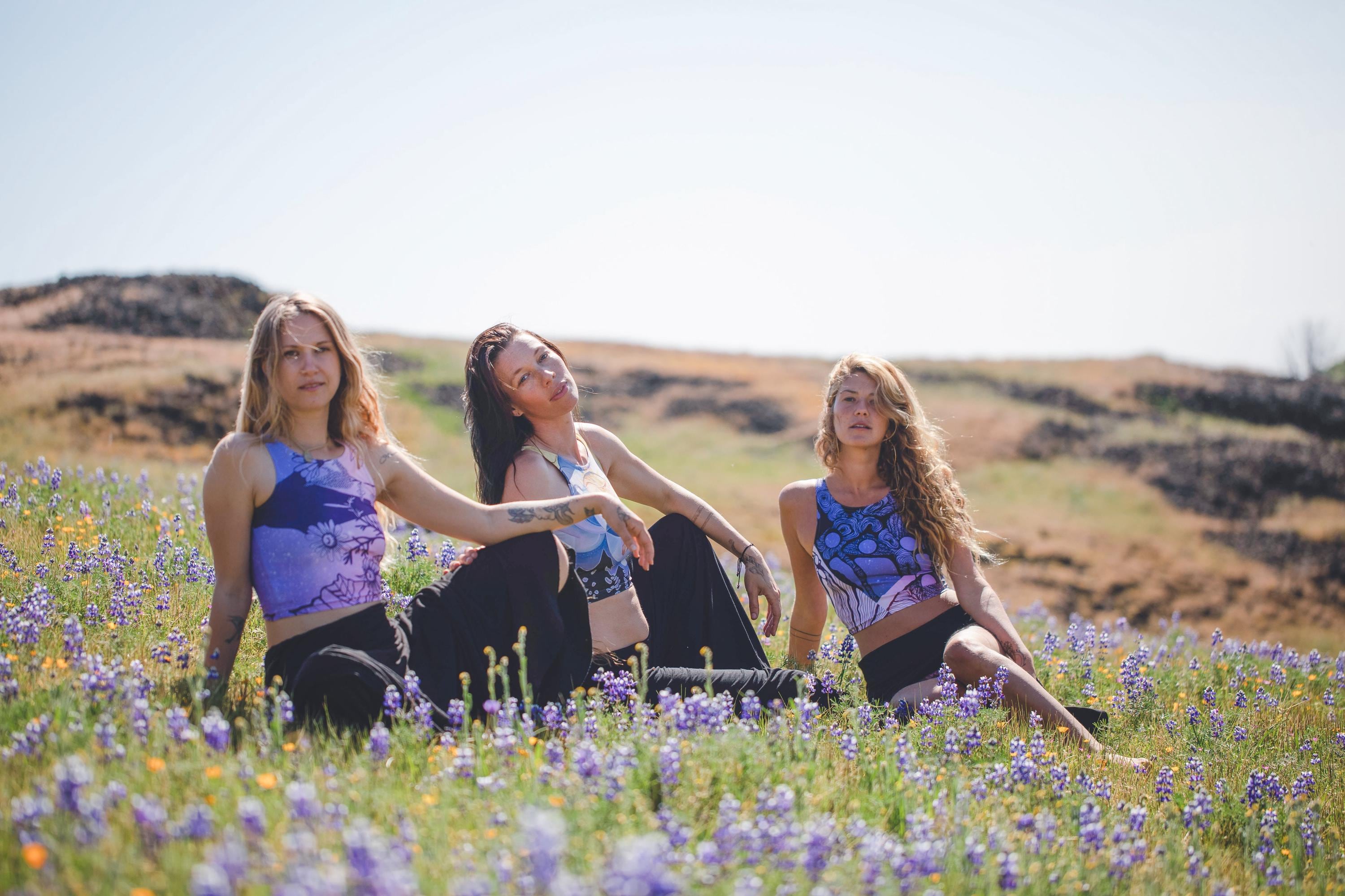 3 women wearing Yoga tops in black blue and purple with back Lines and designs in the shape of moons and a woman next to a tree