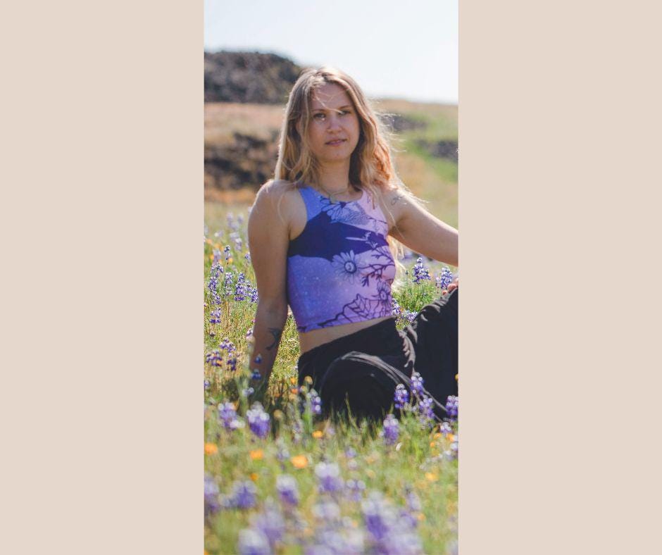 woman wearing Yoga top in shades of pink and purple with plants in black in a field of flowers