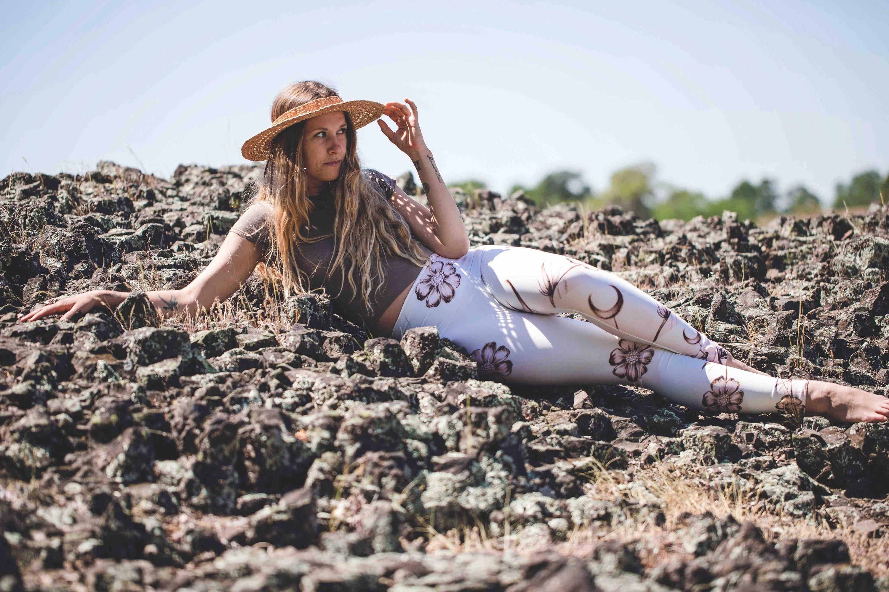 woman laying in Yoga leggings in shades of white and cream with images of flowers and crescent moons drawn on them