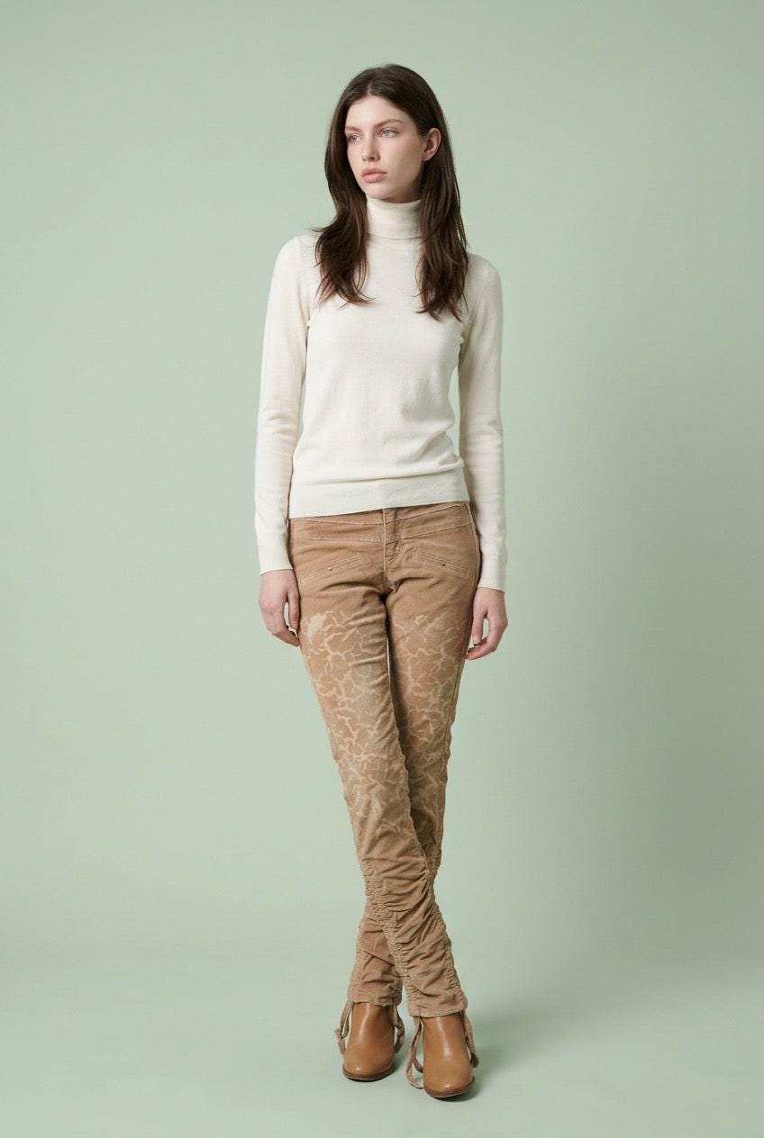 Woman wearing a cream sweater and brown patterned corduroypants on a light green background
