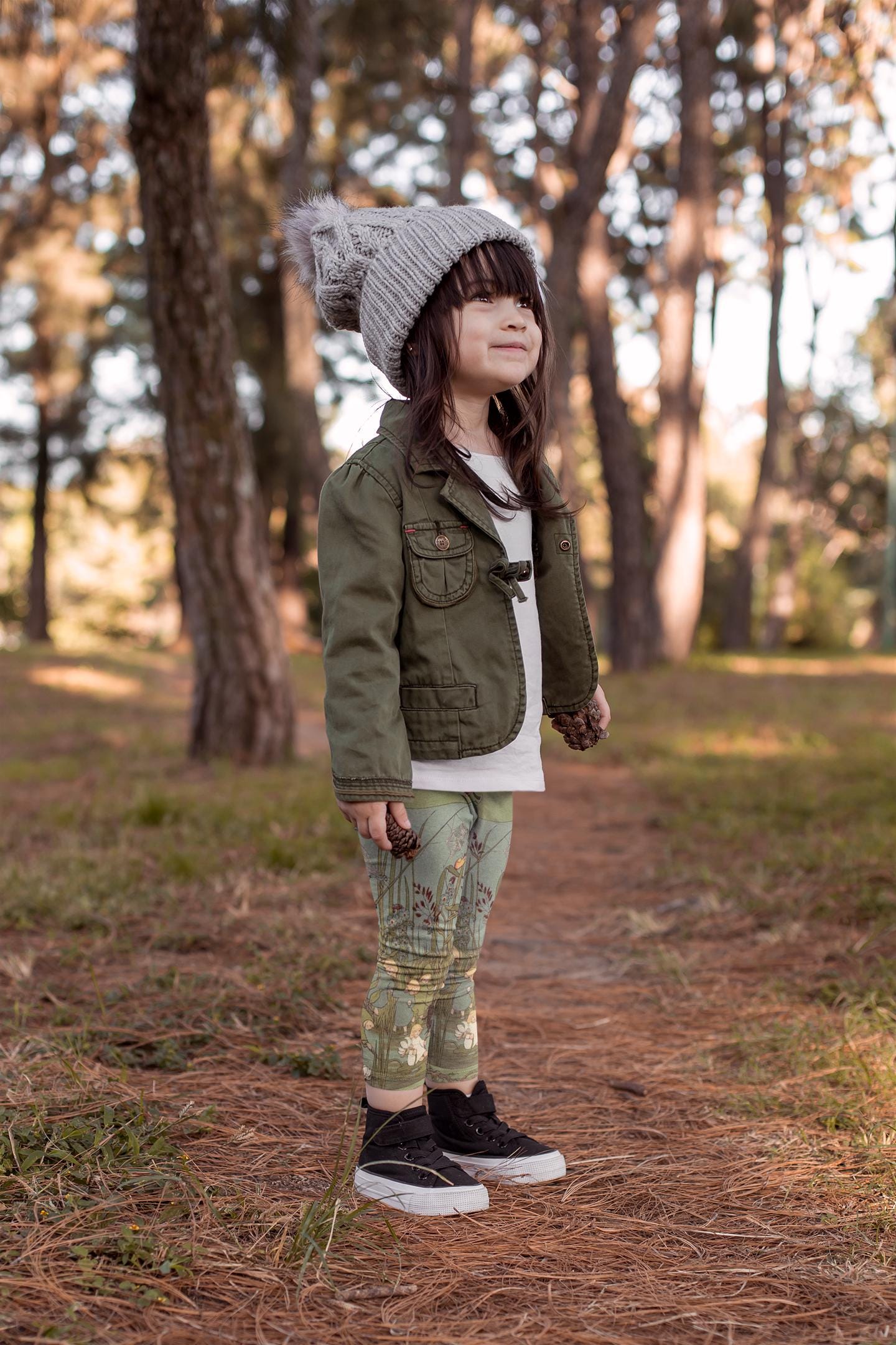 Little girl wearing green and blue illustrated leggings from Elsa beskows the root children. the leggings have images of little flower children in simple clothes and beautiful flowers. they are mostly teal green with some teal blue