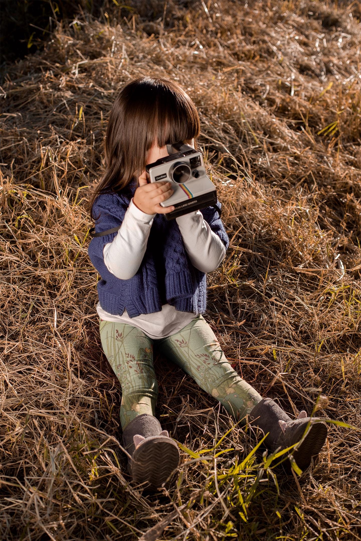Little girl wearing green and blue illustrated leggings from Elsa beskows the root children. the leggings have images of little flower children in simple clothes and beautiful flowers. they are mostly teal green with some teal blue