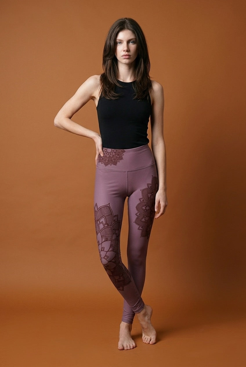Woman wearing black top and purple leggings with lotus mandala lace details on a brown background