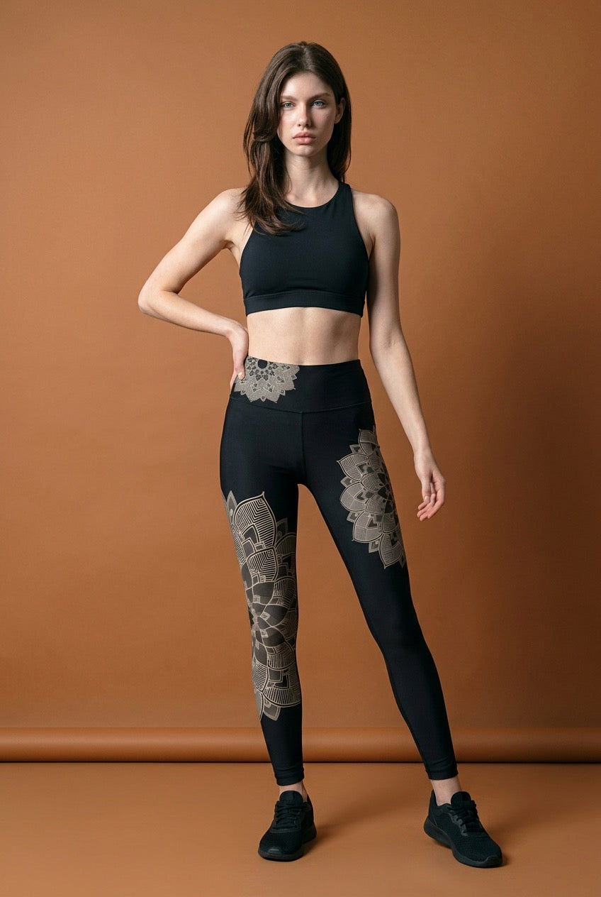 Woman wearing black athletic top and leggings with lotus lace mandala details on a brown background